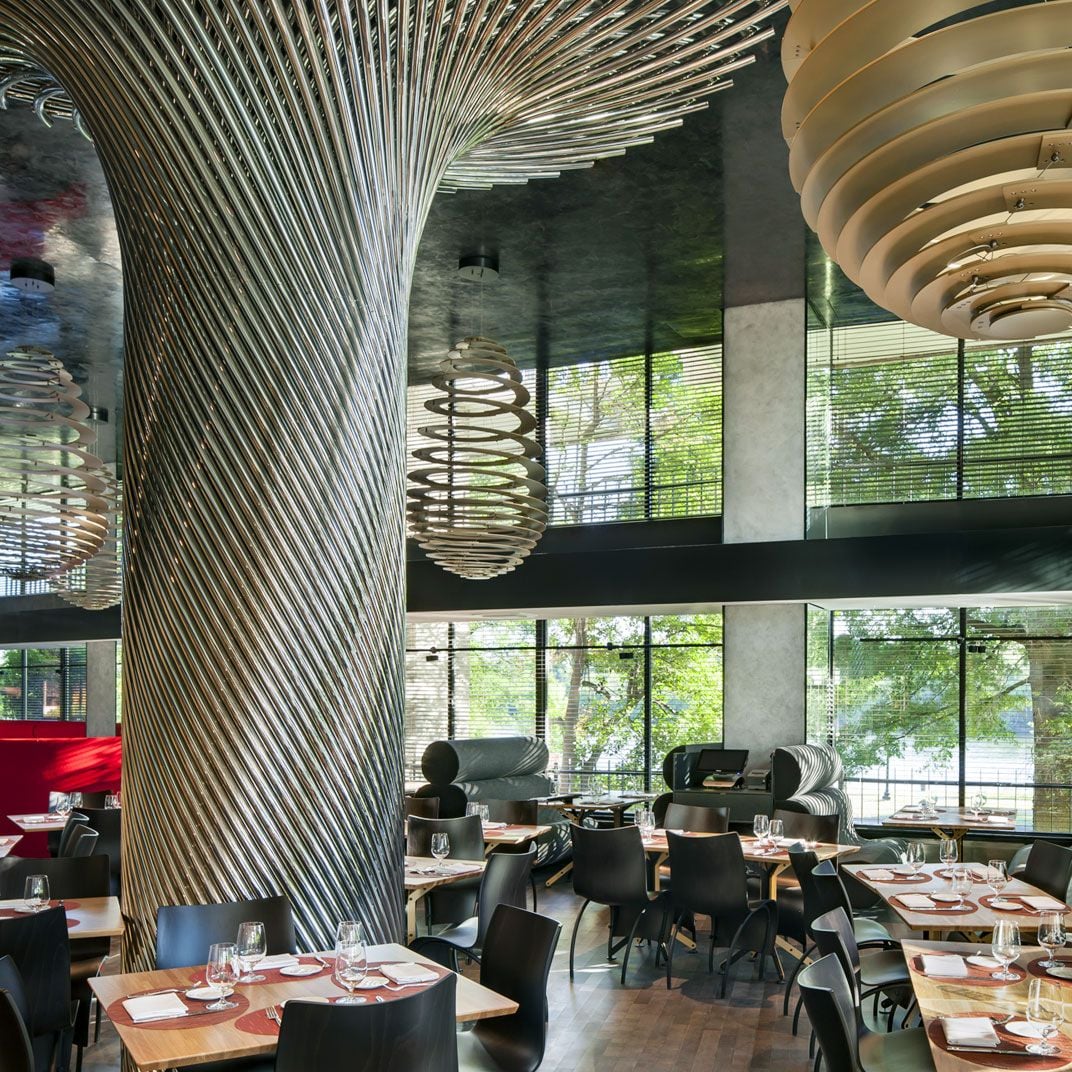 Sculptural metal ribbons spiral dramatically through Kingbird restaurant, where modern pendant lights cast warm glows over intimate tables framed by floor-to-ceiling windows.