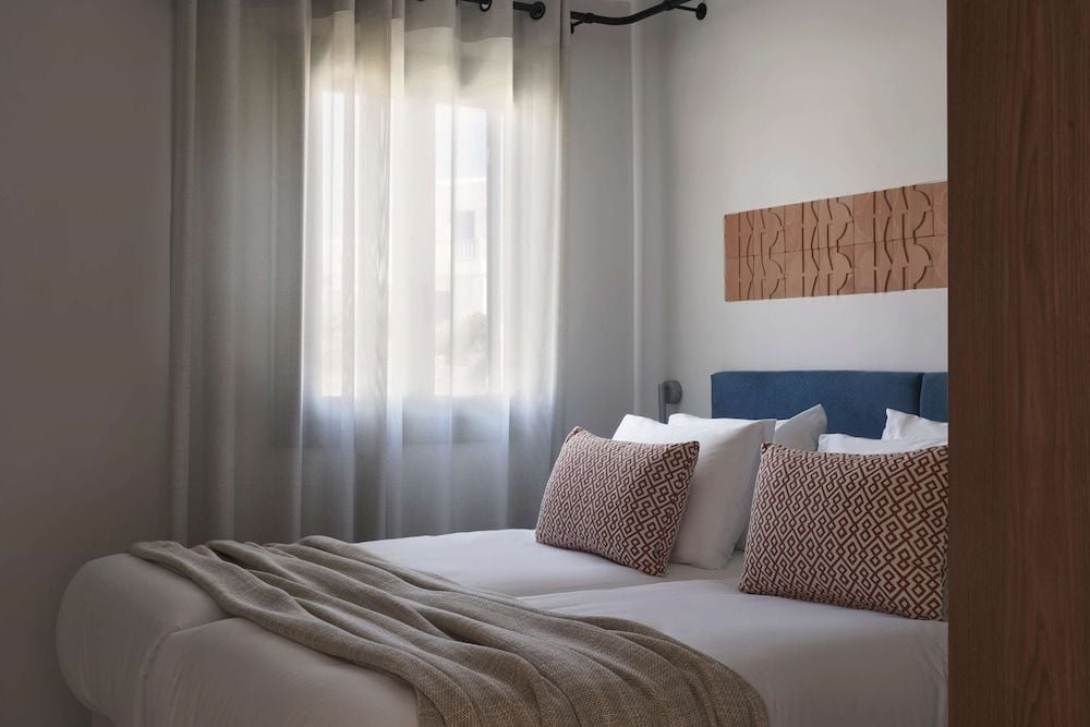 Crisp white linens meet geometric throw pillows in tastefully appointed guest rooms, where natural wood accents and soft afternoon light create an effortlessly sophisticated retreat.