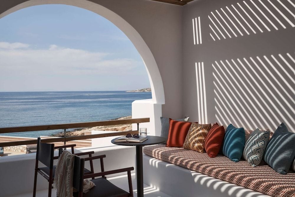 Curved archways frame the endless Aegean while shadows dance across plush cushions, creating an intimate sanctuary where sea breezes carry the scent of sun-warmed stone.