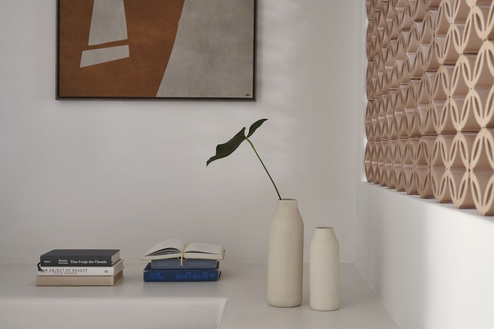 Minimalist ceramic vases and carefully curated books create intimate vignettes against sculptural wall treatments, embodying the hotel's refined Cycladic aesthetic.