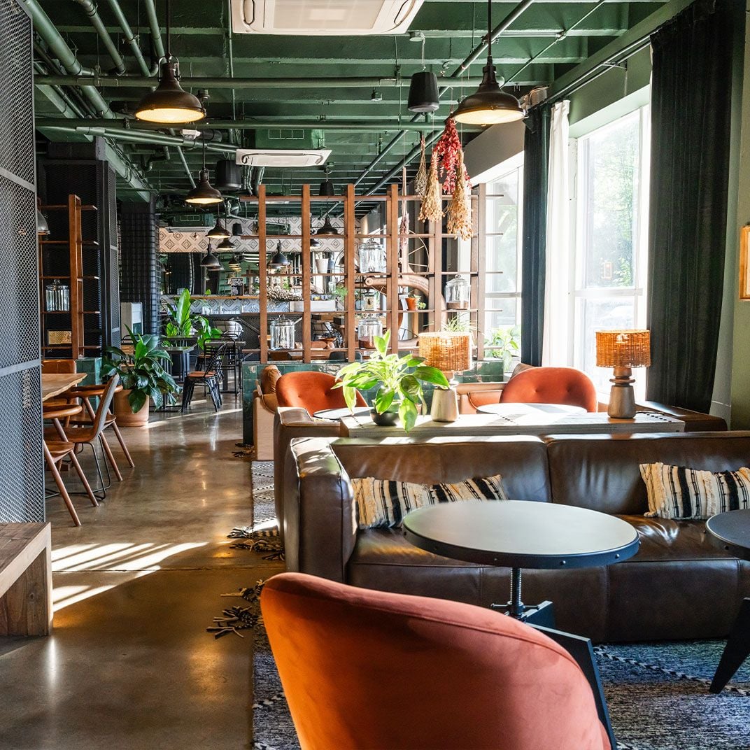 Industrial pendant lights cast warm pools over velvet armchairs and leather banquettes, while exposed green ceiling pipes add urban edge to this inviting social hub.