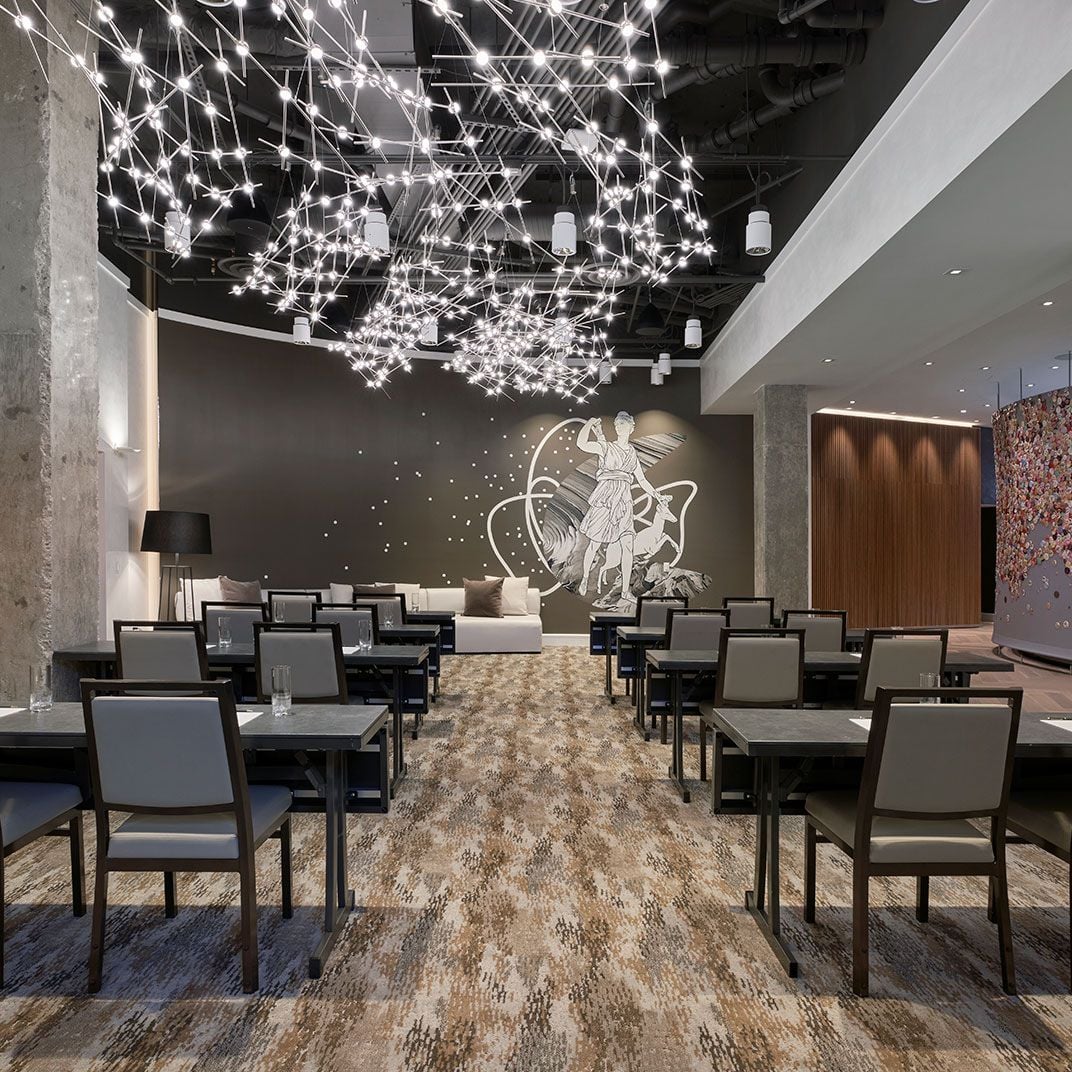 Sculptural light installations dance overhead while mythological wall art creates drama in this sophisticated dining space where modern design meets celestial inspiration.