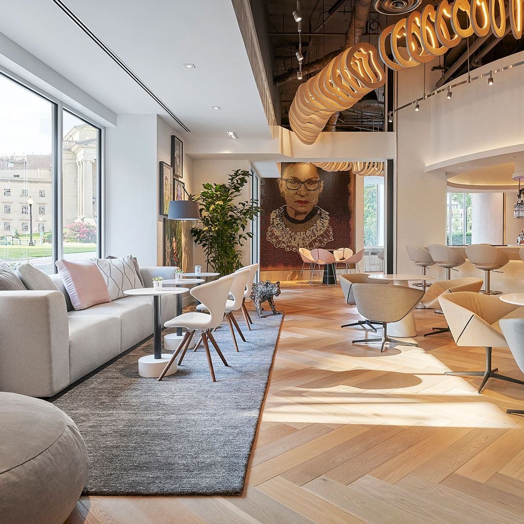 Sculptural wood installations spiral overhead while Ruth Bader Ginsburg's portrait anchors this sophisticated lobby, where mid-century chairs and contemporary art create an empowering atmosphere.