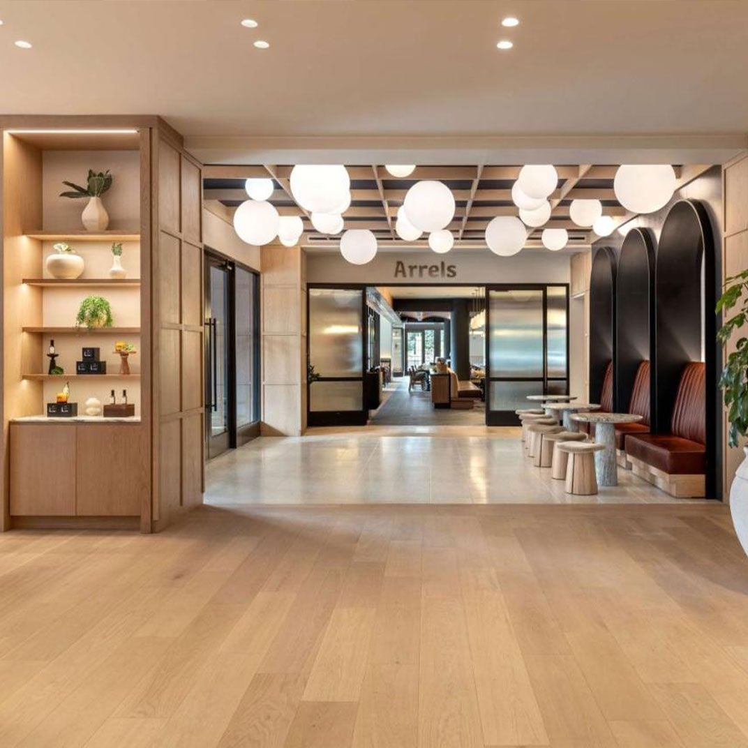 Warm wood shelving displays curated objects while spherical pendant lights float overhead, creating an inviting arrival experience that feels more boutique residence than traditional hotel.