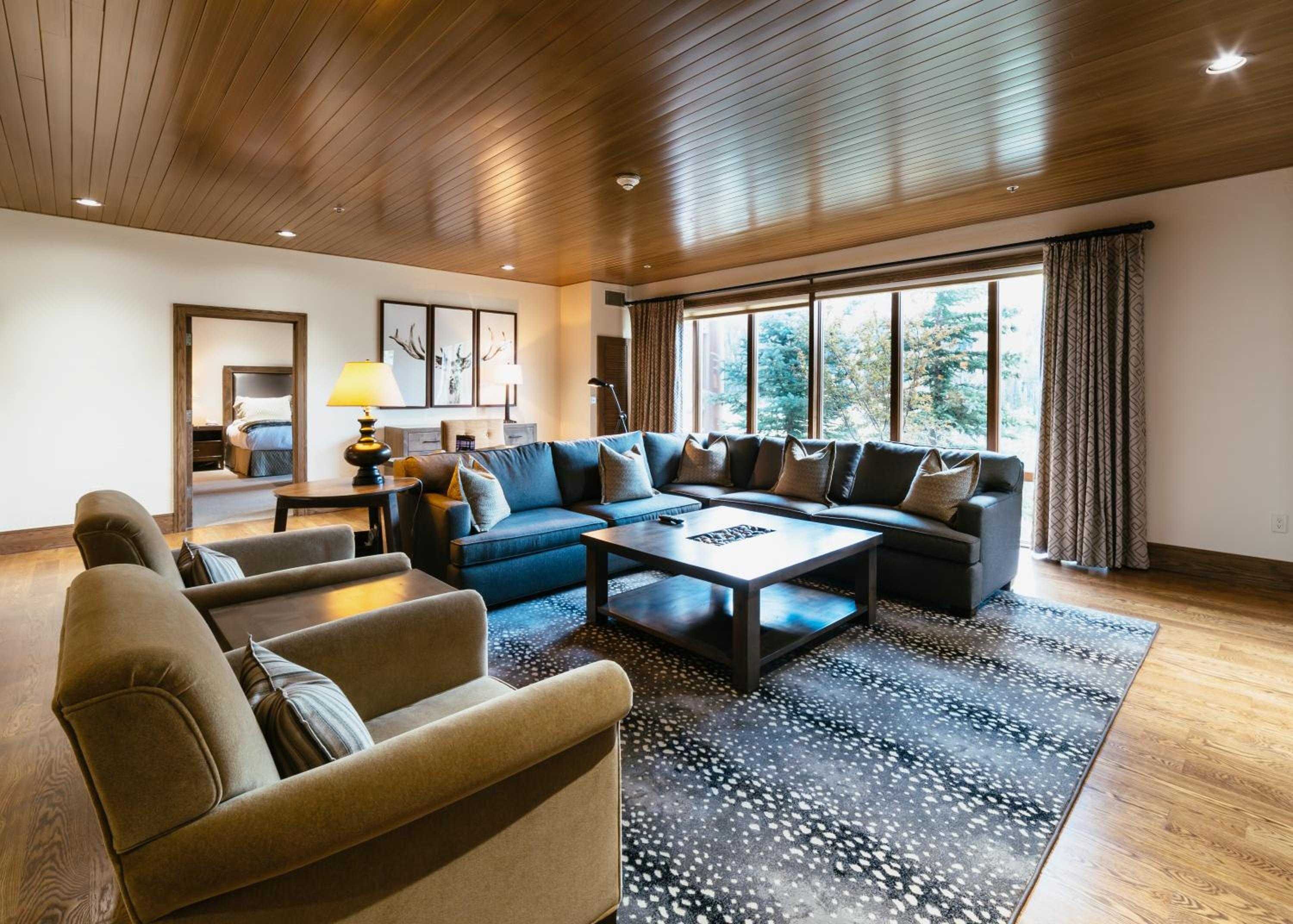 Warm wood ceilings and contemporary mountain furnishings create an inviting retreat, where floor-to-ceiling windows frame Utah's alpine landscape beyond plush sectional seating.