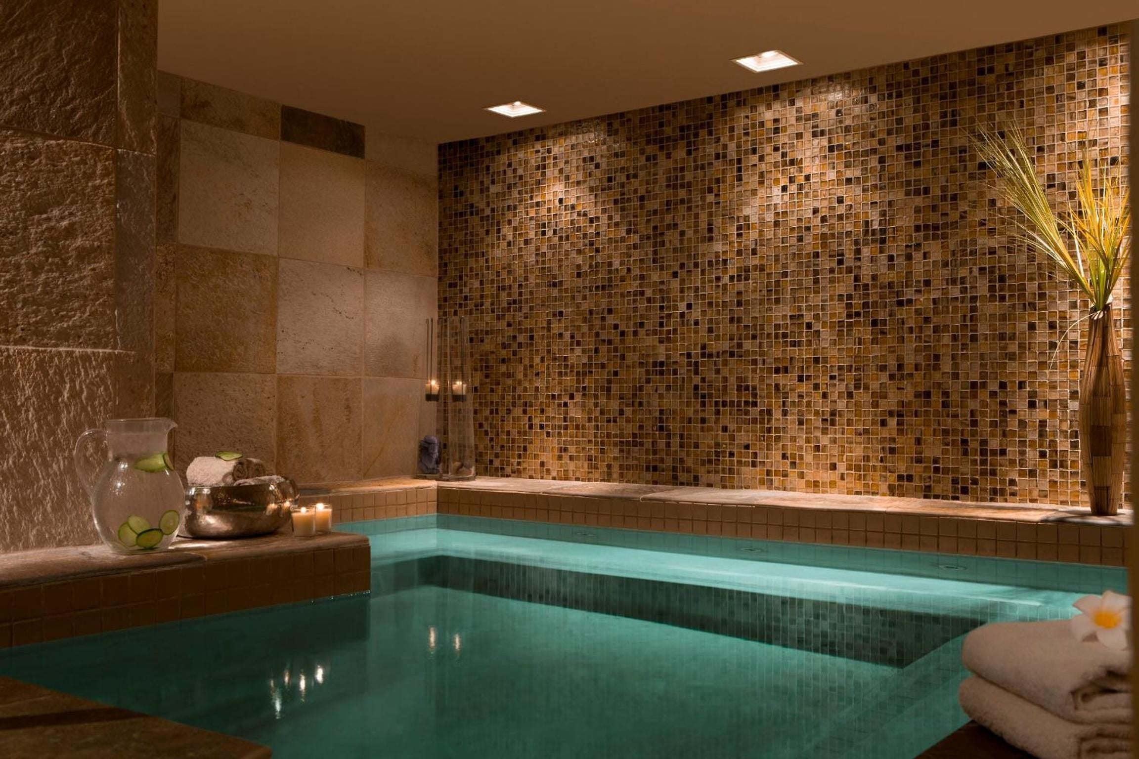 Candlelit mosaic tiles in warm amber hues create an intimate grotto atmosphere around the sunken soaking pool, where heated waters invite deep relaxation.