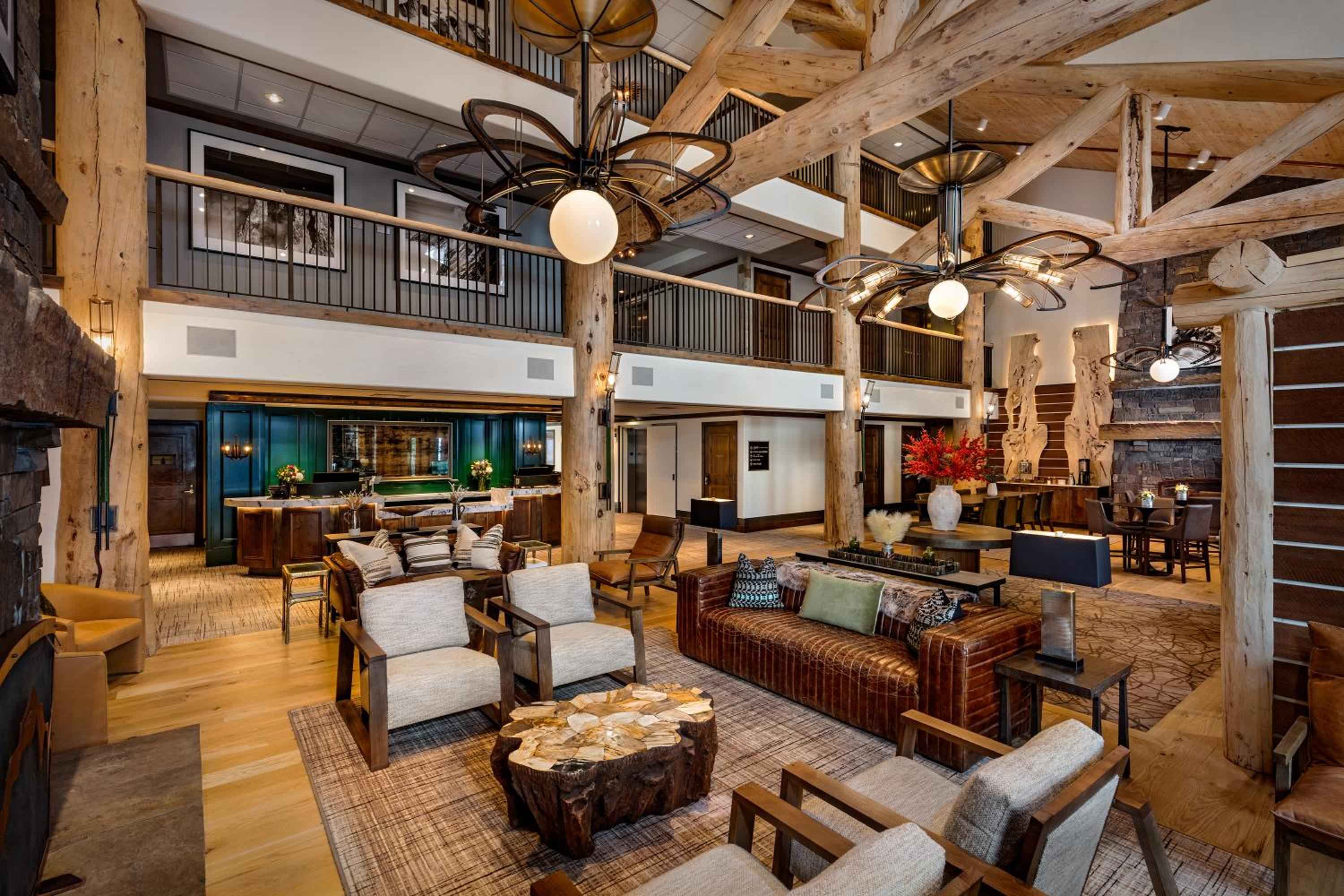 Soaring timber beams and wrought-iron balconies frame this grand mountain lodge lobby, where leather sofas and rustic wood tables invite lingering by the contemporary fireplace.