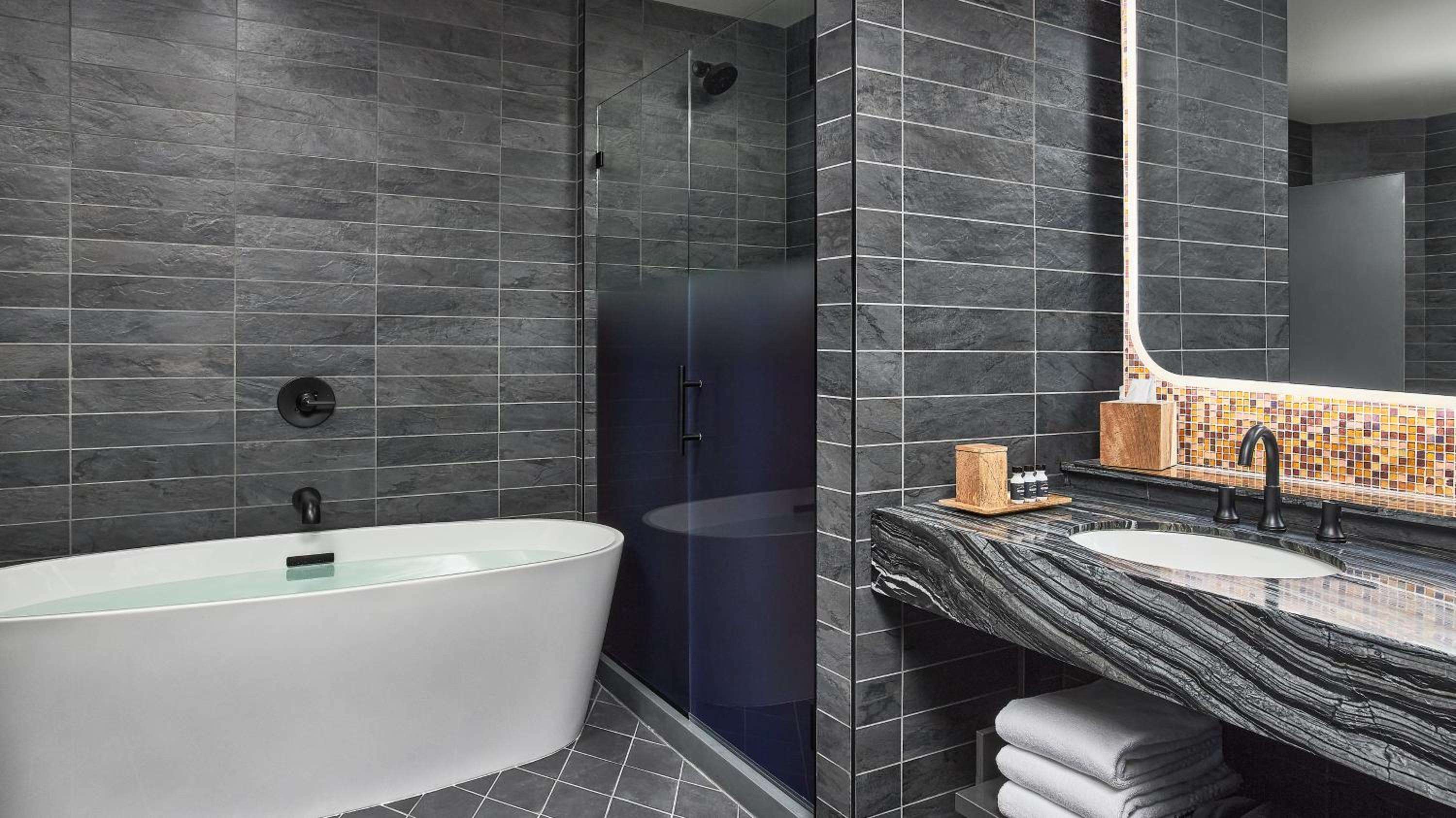 Charcoal slate tiles and dramatic veined marble create a spa-like sanctuary, where the freestanding soaking tub invites long, contemplative soaks after game day excitement.