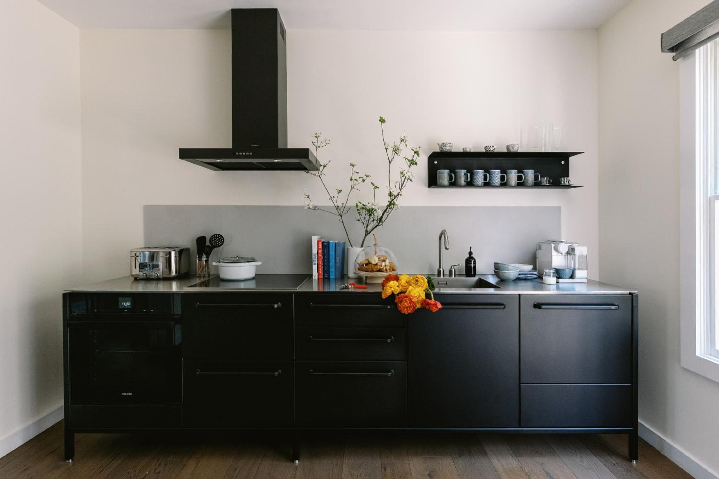 Sleek black cabinetry and stainless steel surfaces create a sophisticated galley kitchen, where fresh marigolds and carefully curated cookbooks add warmth to the minimalist design.
