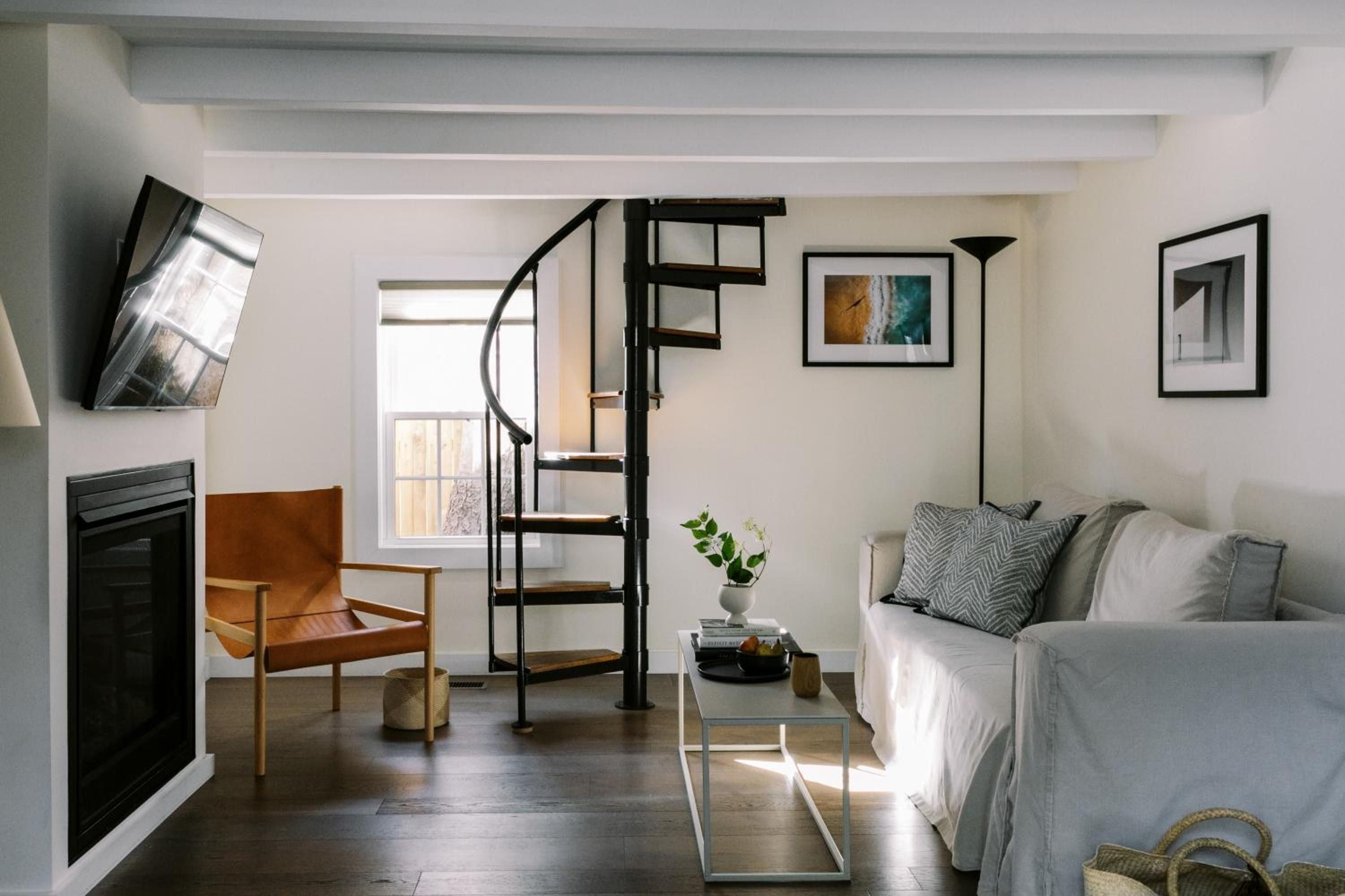 Exposed beams frame this thoughtfully appointed suite, where a sculptural spiral staircase leads upward and mid-century furnishings create an effortlessly sophisticated retreat.