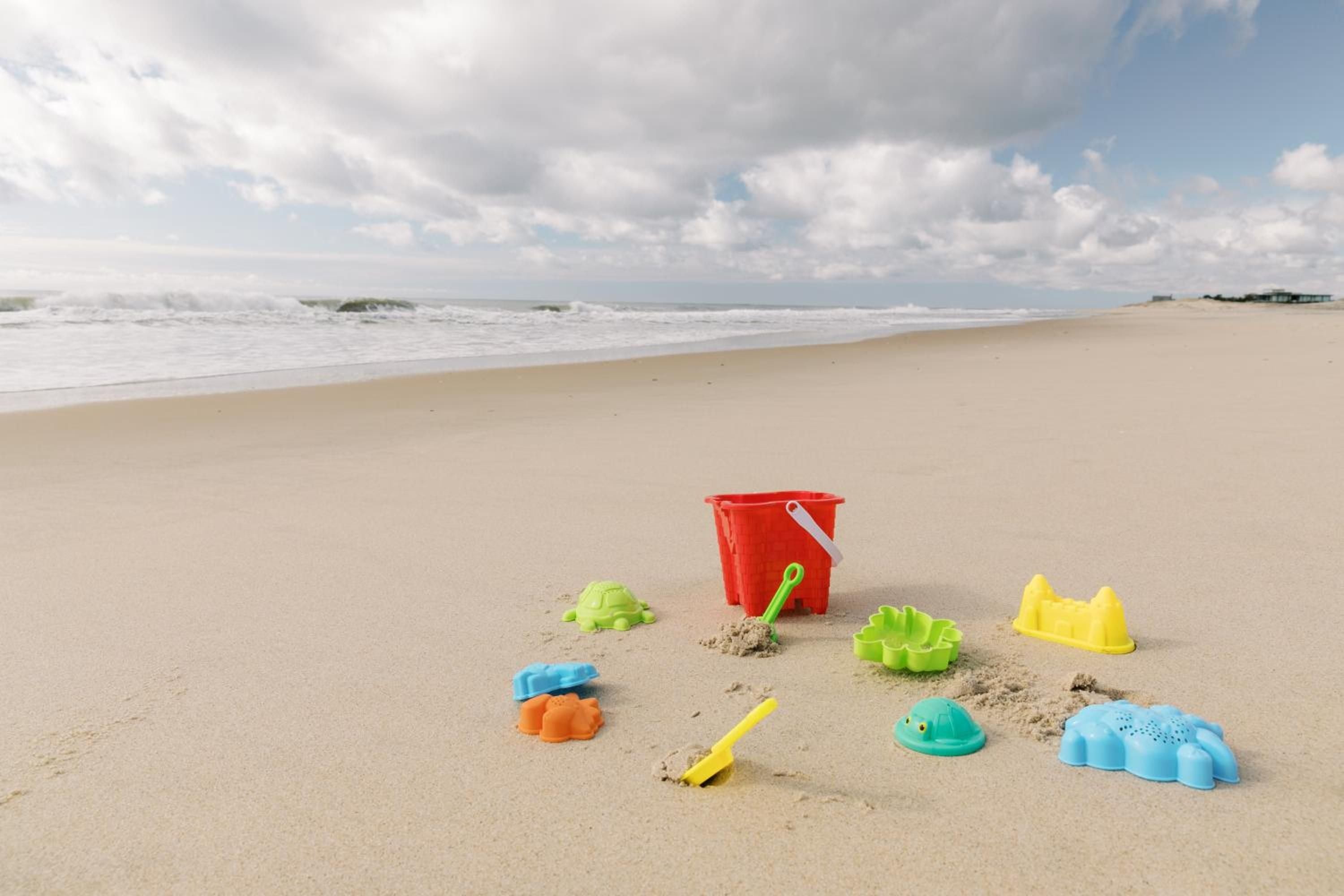 Colorful sand toys scattered across pristine Amagansett shore promise endless childhood adventures, while gentle waves and cloudy skies create the perfect backdrop for family memories.