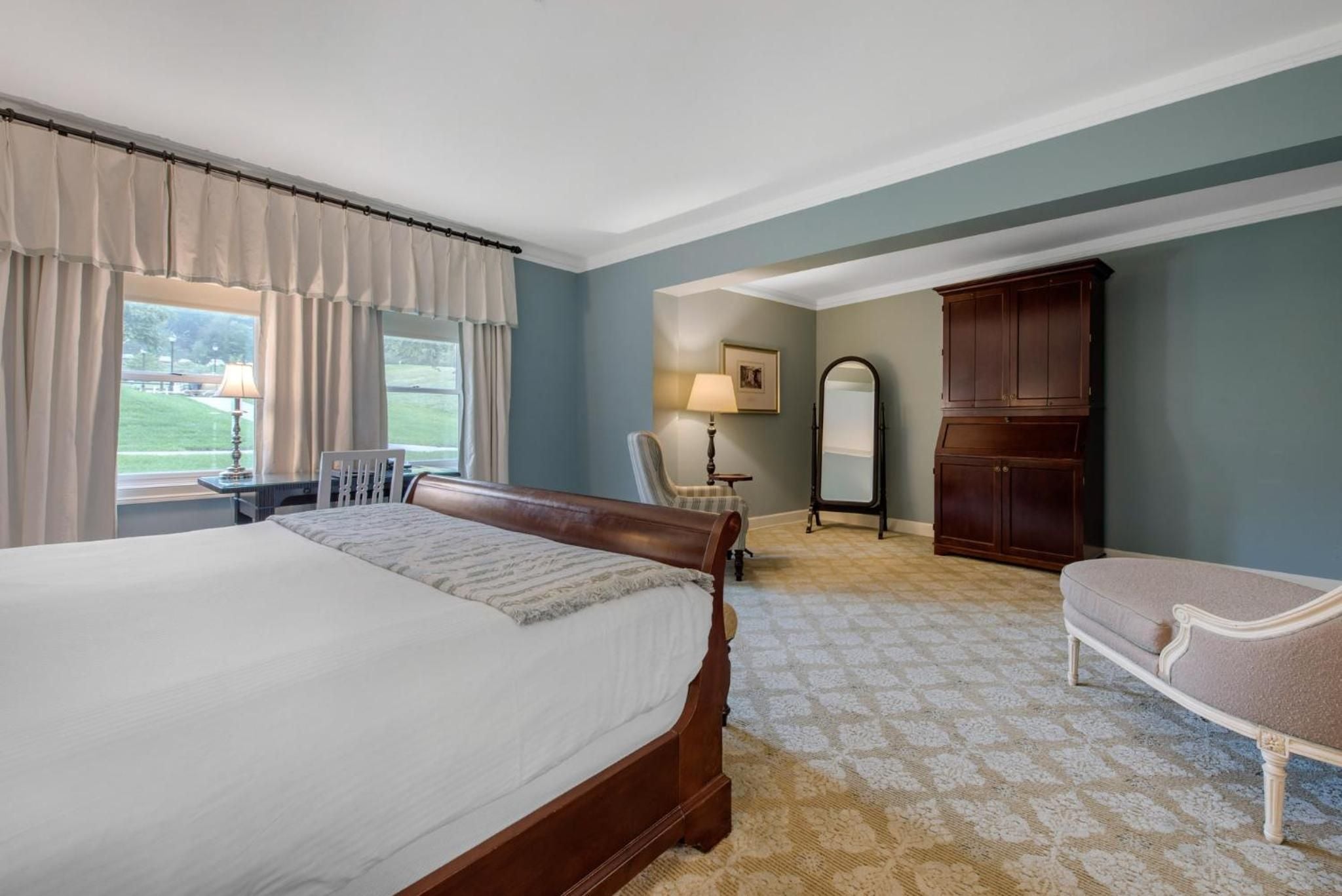 Sage-green walls and rich mahogany furnishings create an intimate sanctuary, where morning light filters through cream curtains onto plush carpeting and traditional sleigh beds.