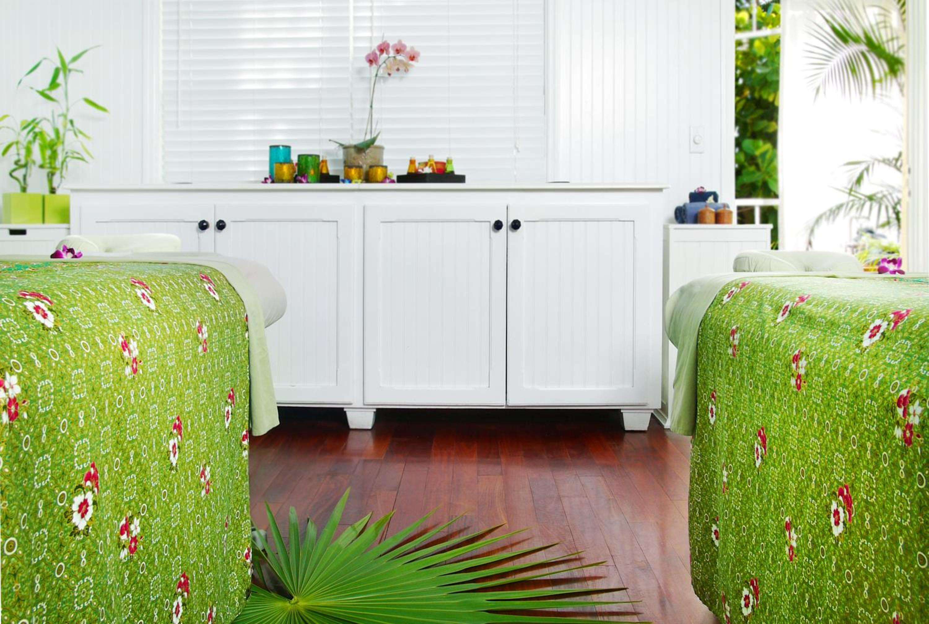 Side-by-side treatment tables draped in vibrant tropical linens create an intimate couples spa experience, where orchids and natural light enhance the serene atmosphere.