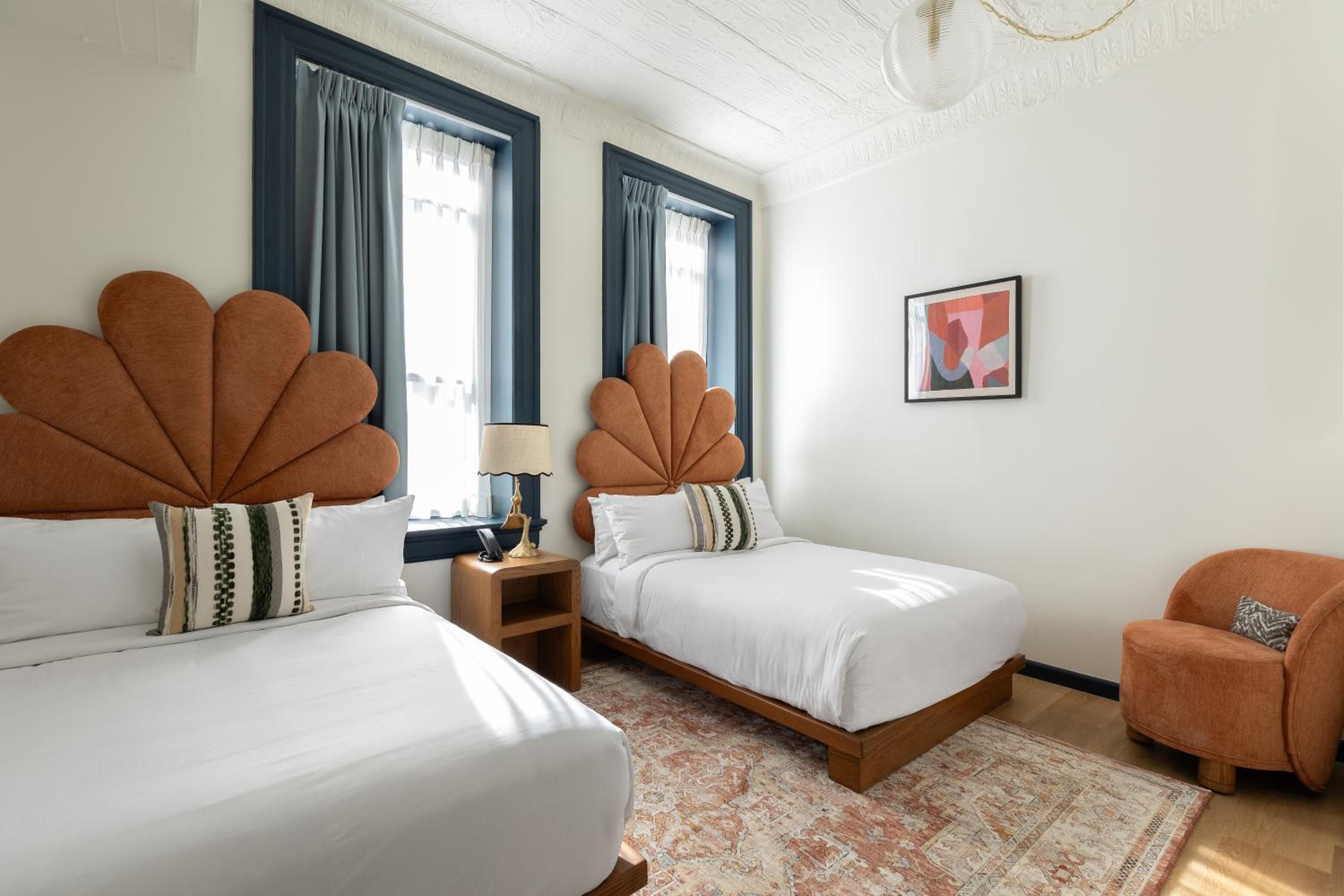 Twin beds crowned with distinctive scalloped headboards create a playful yet sophisticated sanctuary, where terracotta tones meet crisp white linens under natural light.
