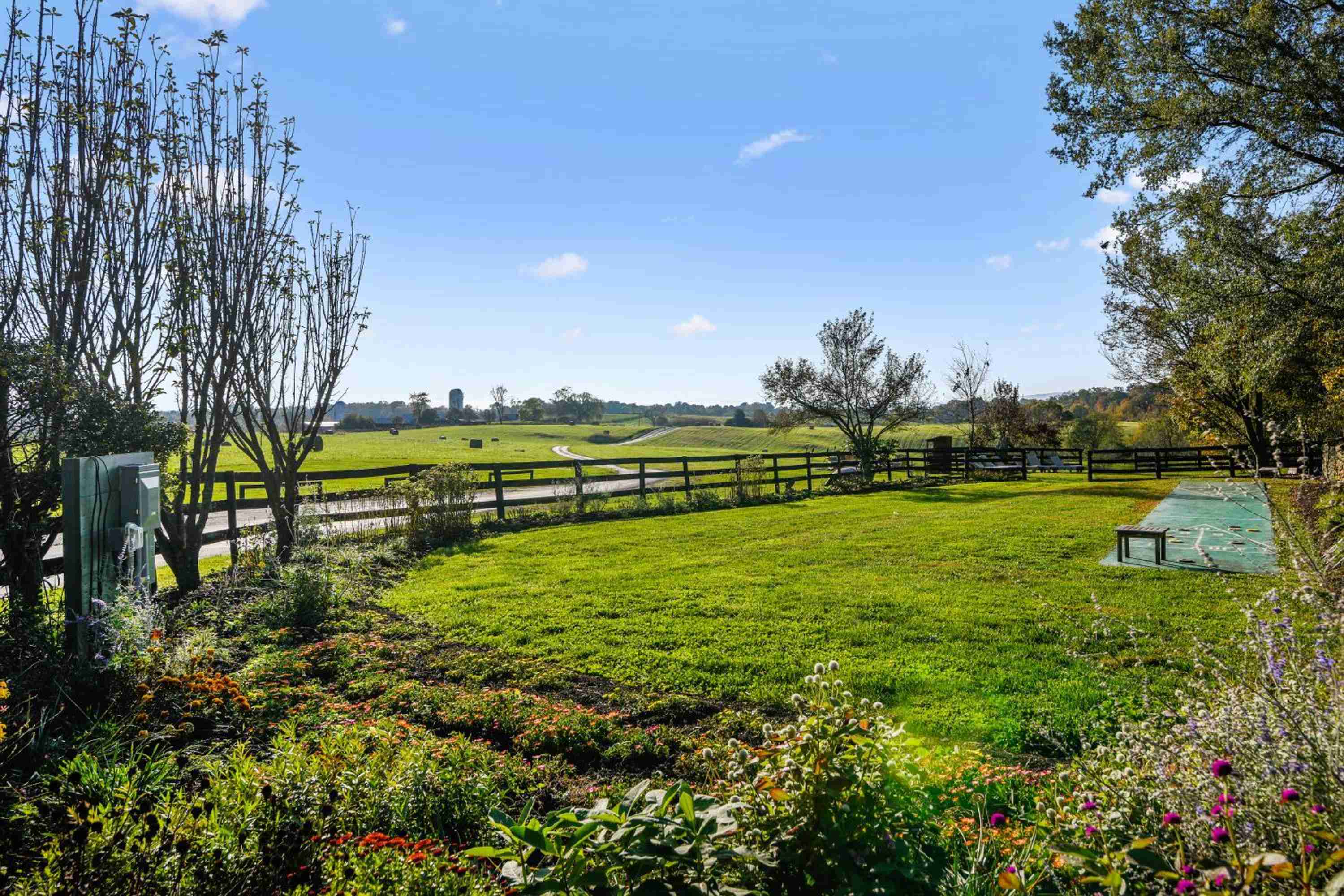 Rolling pastures stretch beyond manicured gardens where autumn blooms frame weathered fence posts, creating an idyllic countryside tableau that epitomizes Virginia's pastoral elegance.