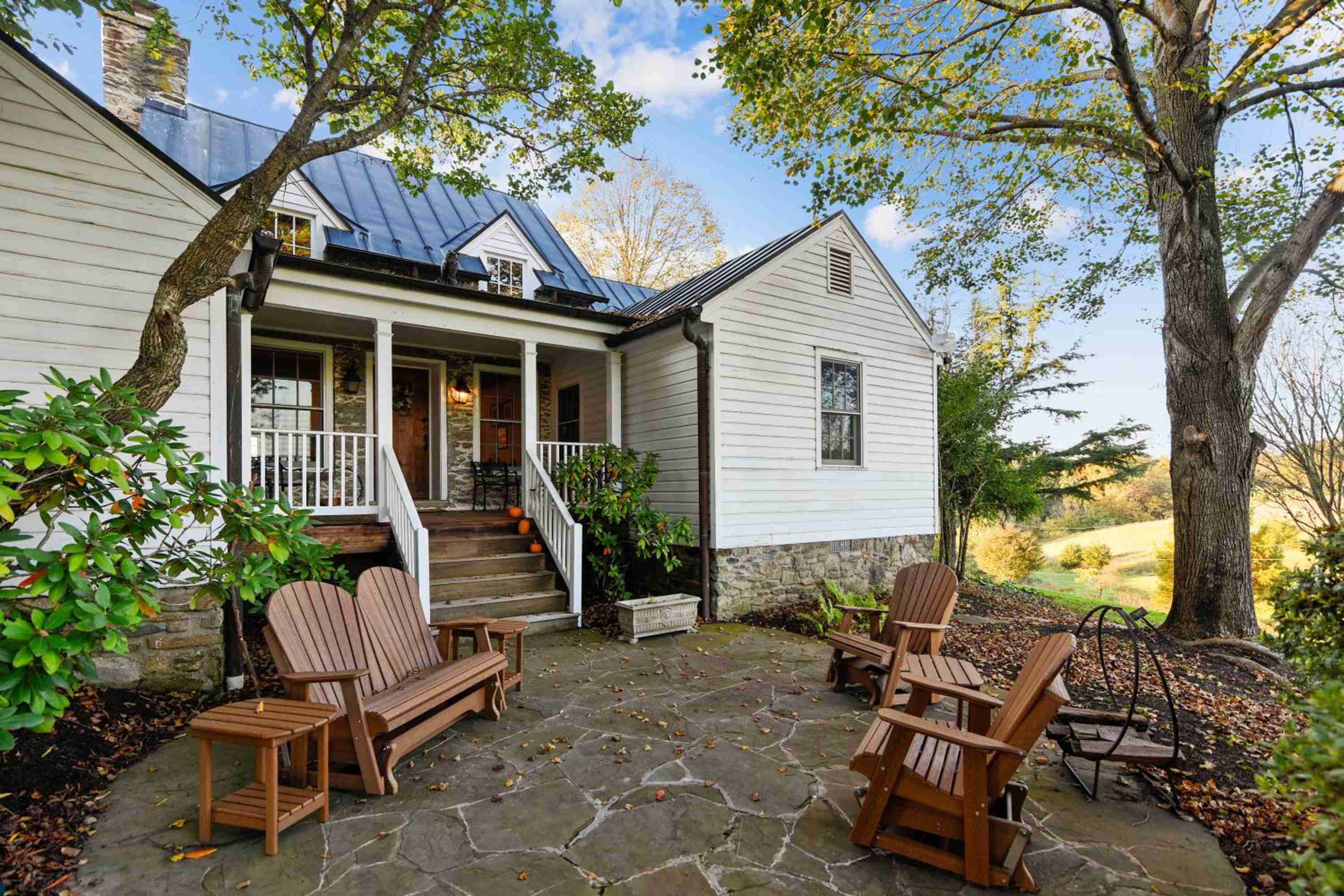 Weathered stone patios and handcrafted Adirondack chairs create intimate gathering spaces beneath century-old oaks, where Virginia countryside views stretch beyond manicured gardens.