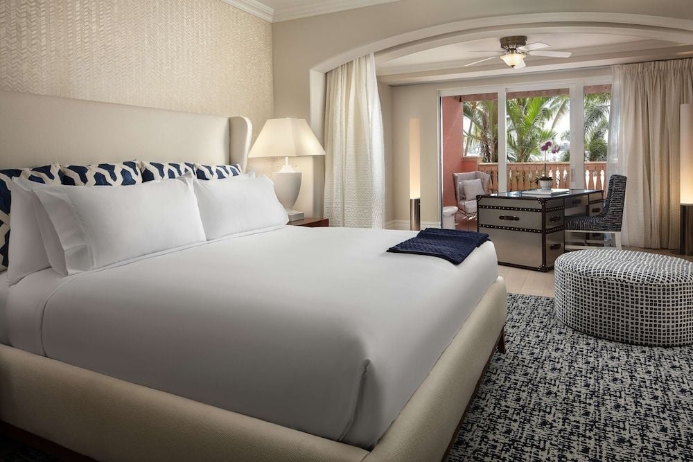 Crisp white linens meet navy geometric accents in this serene suite, where natural light streams across textured walls toward a private balcony overlooking swaying palms.