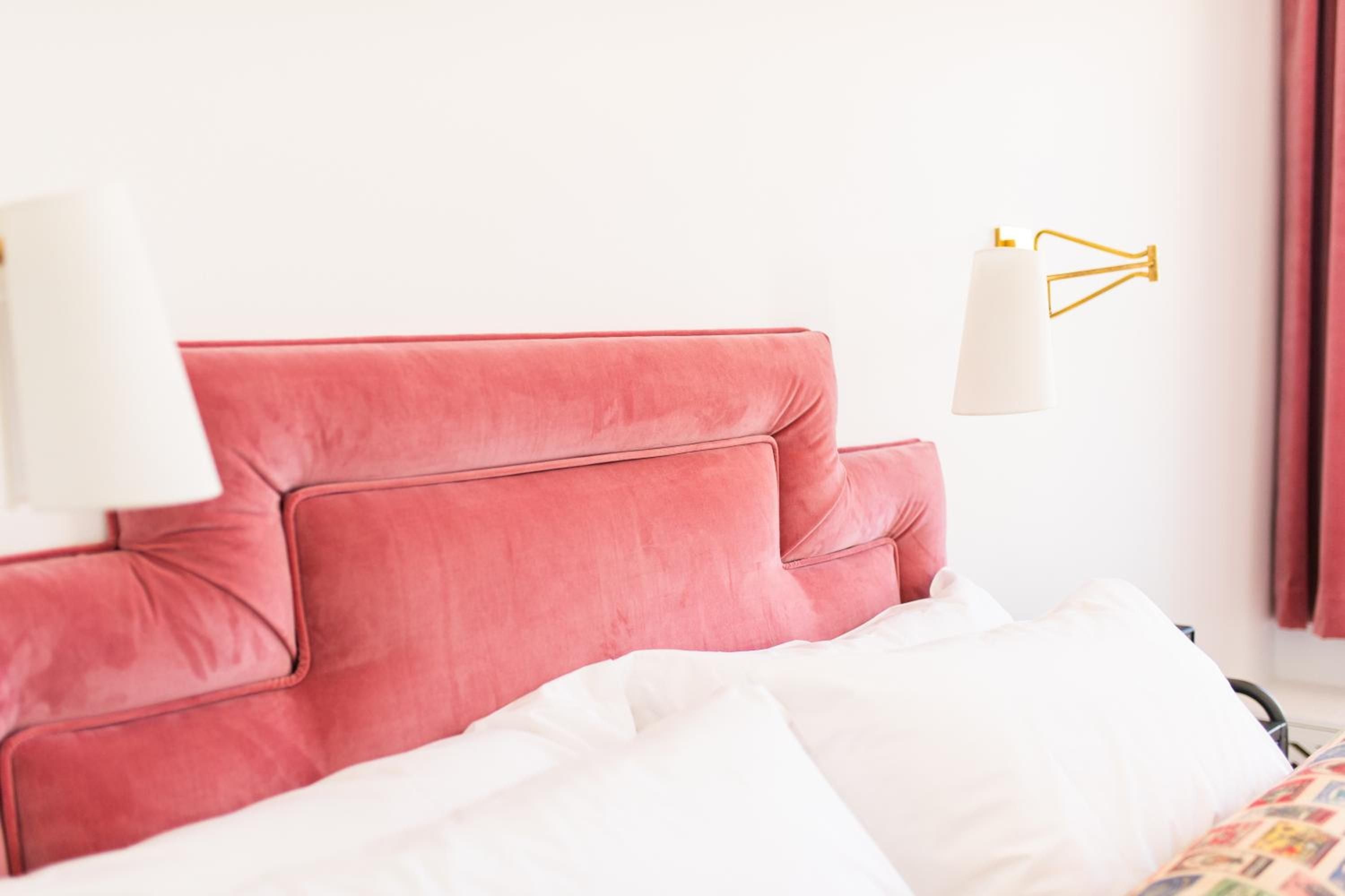 Coral-hued velvet headboards and brass accents create an intimate sanctuary where soft morning light filters through, casting everything in a warm, romantic glow.