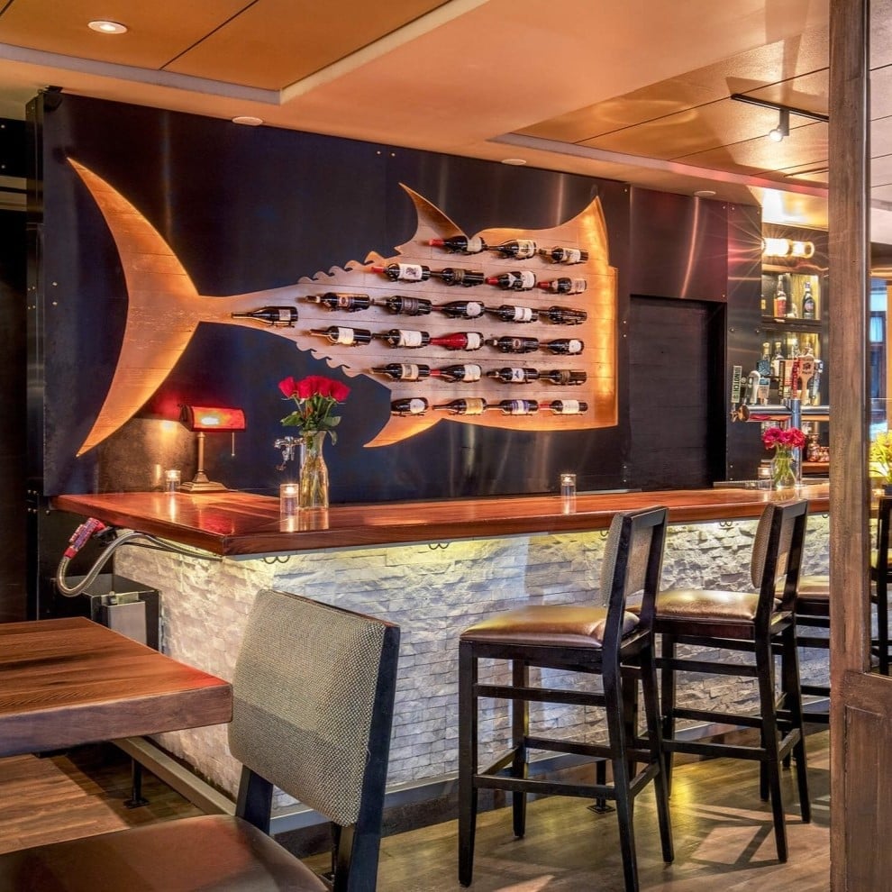 A striking fish-shaped wine rack commands attention at the bar, where warm wood tones and intimate lighting create an inviting atmosphere for evening conversations.