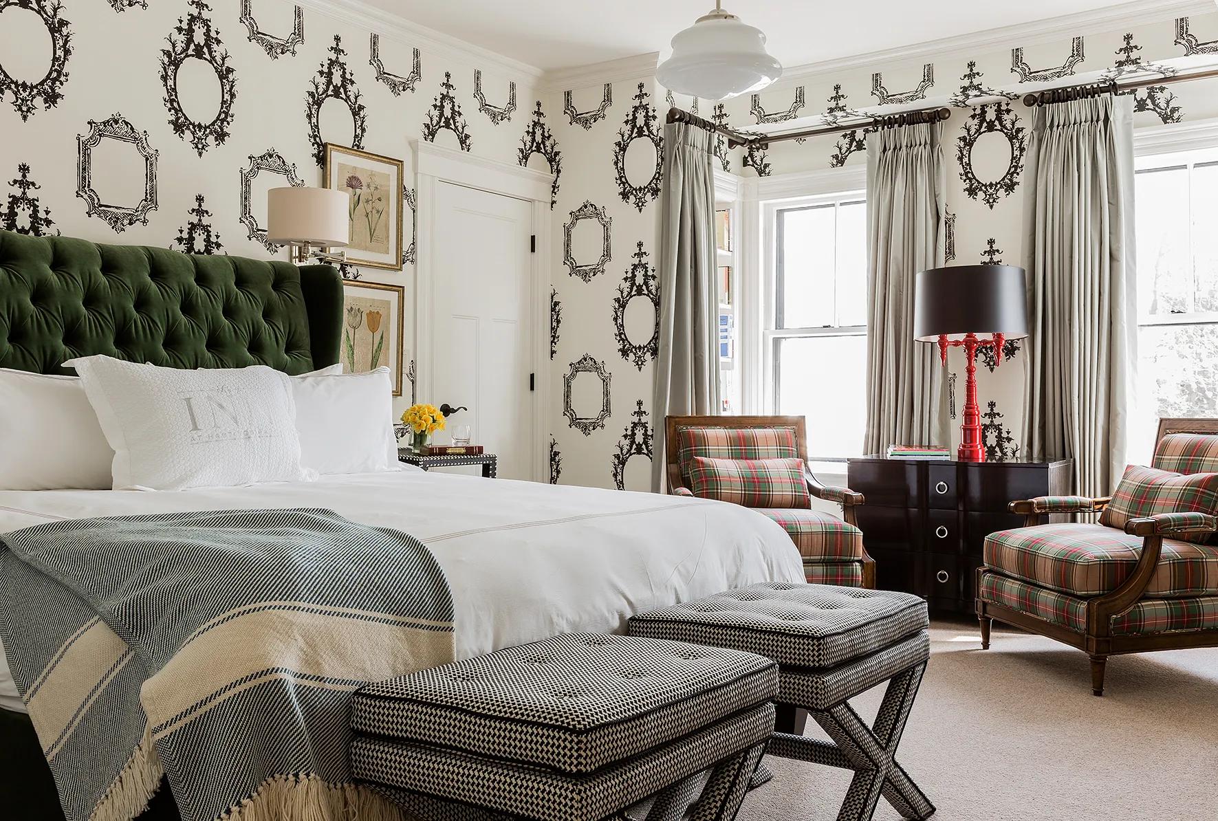 Whimsical mirror-motif wallpaper meets emerald velvet tufting in this sophisticated guest room, where plaid armchairs and striped throws create layers of refined New England charm.