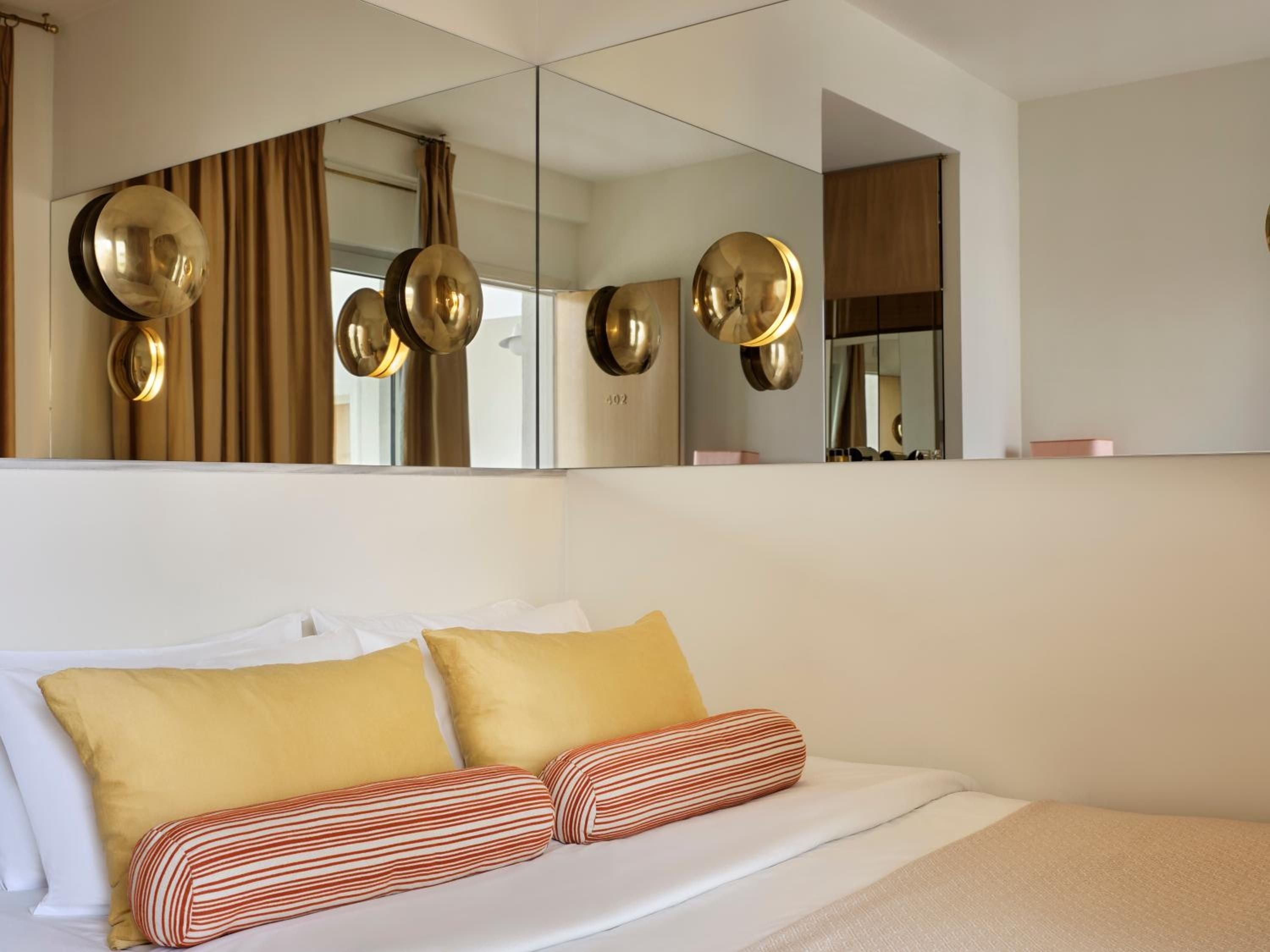 Golden spherical sconces cast warm light across crisp linens, while striped bolster pillows add playful geometry to this thoughtfully designed retreat.