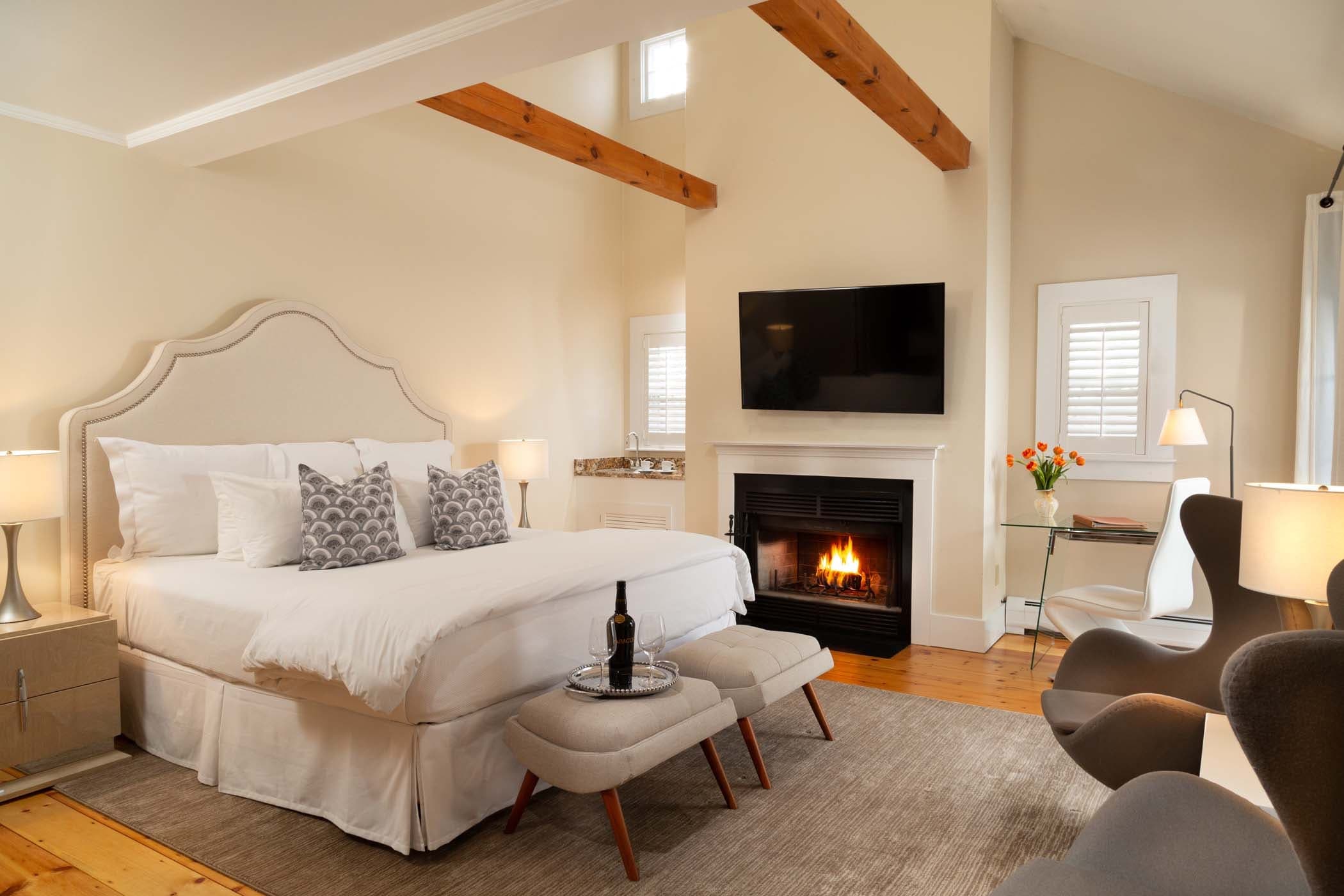 Exposed wooden beams frame this intimate guest room where crackling fireplace flames dance beneath a wall-mounted television, creating perfect après-exploration ambiance.