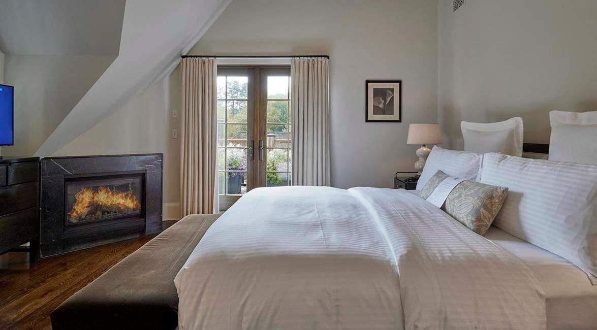 Flickering flames cast a warm glow across crisp white linens and honey-toned hardwood floors in this intimate attic suite, where slanted ceilings create cozy sanctuary vibes.