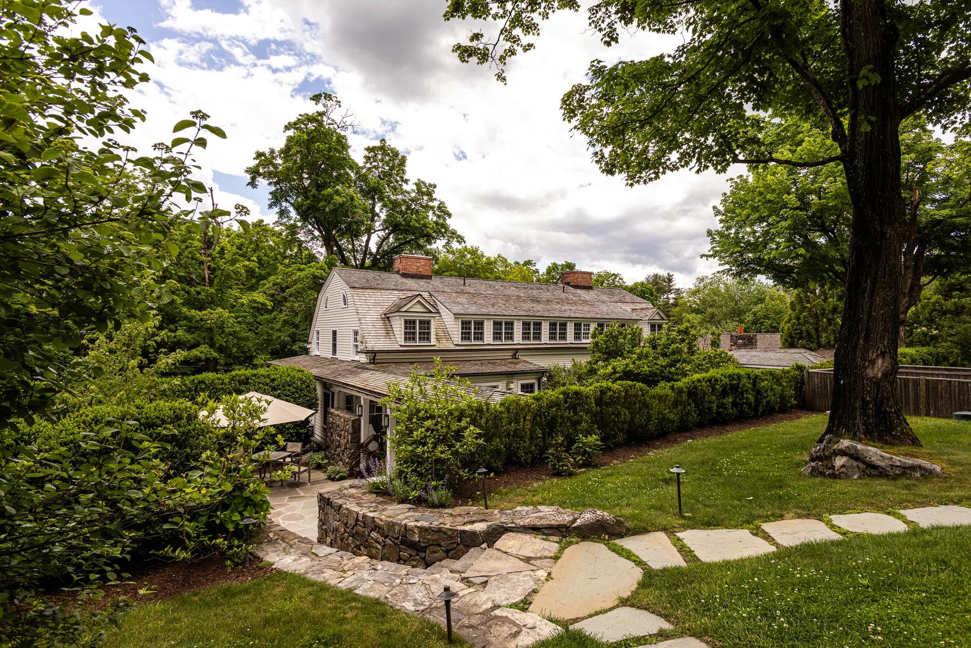 Stone pathways wind through manicured gardens toward the colonial-style main house, where mature trees and rolling lawns create an intimate New England estate atmosphere.