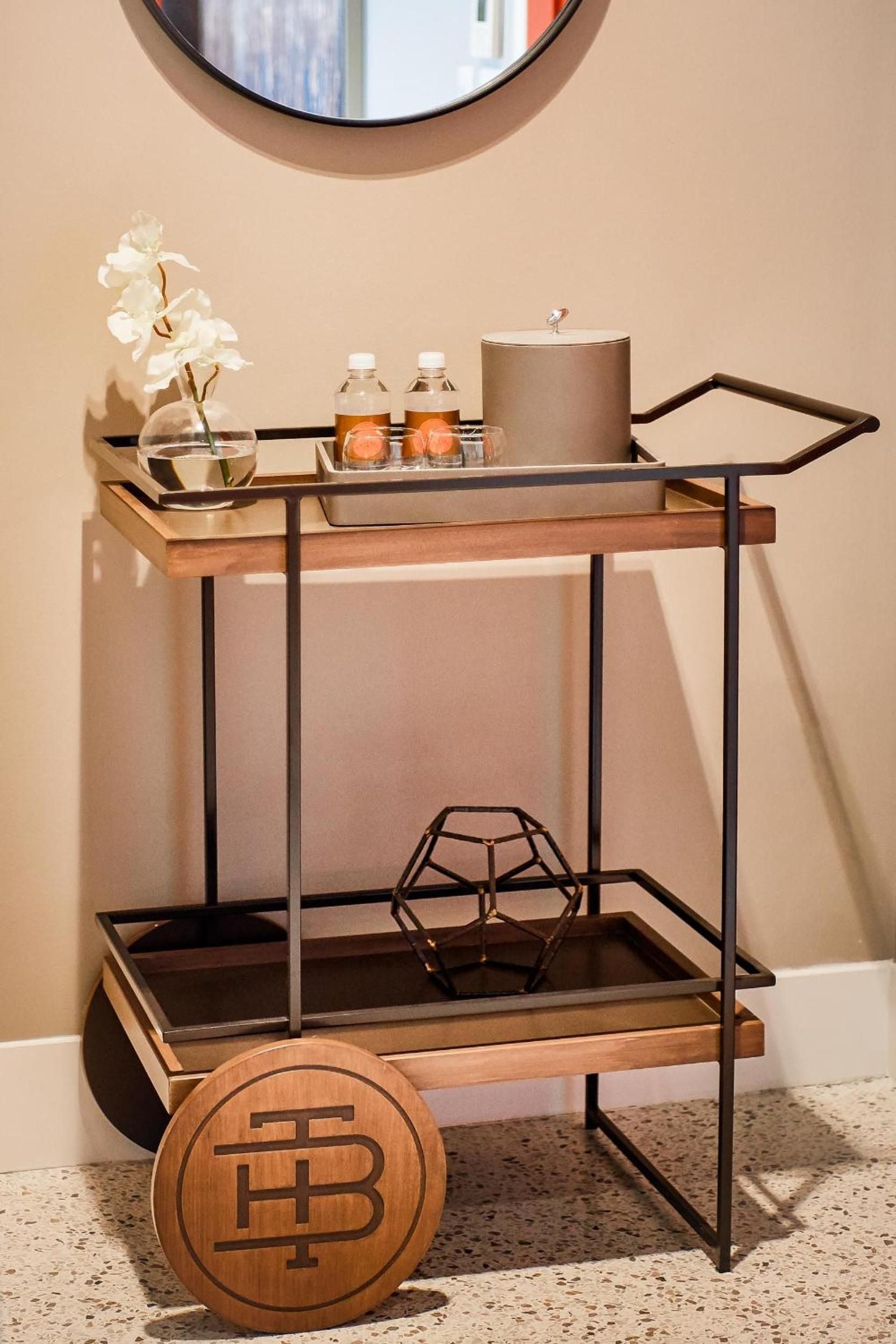 Warm brass and blackened steel create sophisticated contrast on this thoughtfully appointed bar cart, where geometric accessories and fresh orchids add refined touches to guest accommodations.