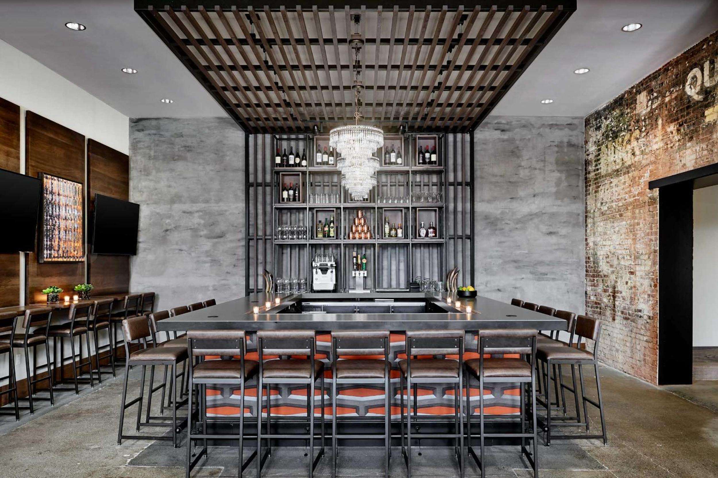 Industrial steel shelving frames premium spirits while a crystal chandelier adds glamour to this sophisticated bar, where exposed brick meets polished concrete in perfect urban harmony.