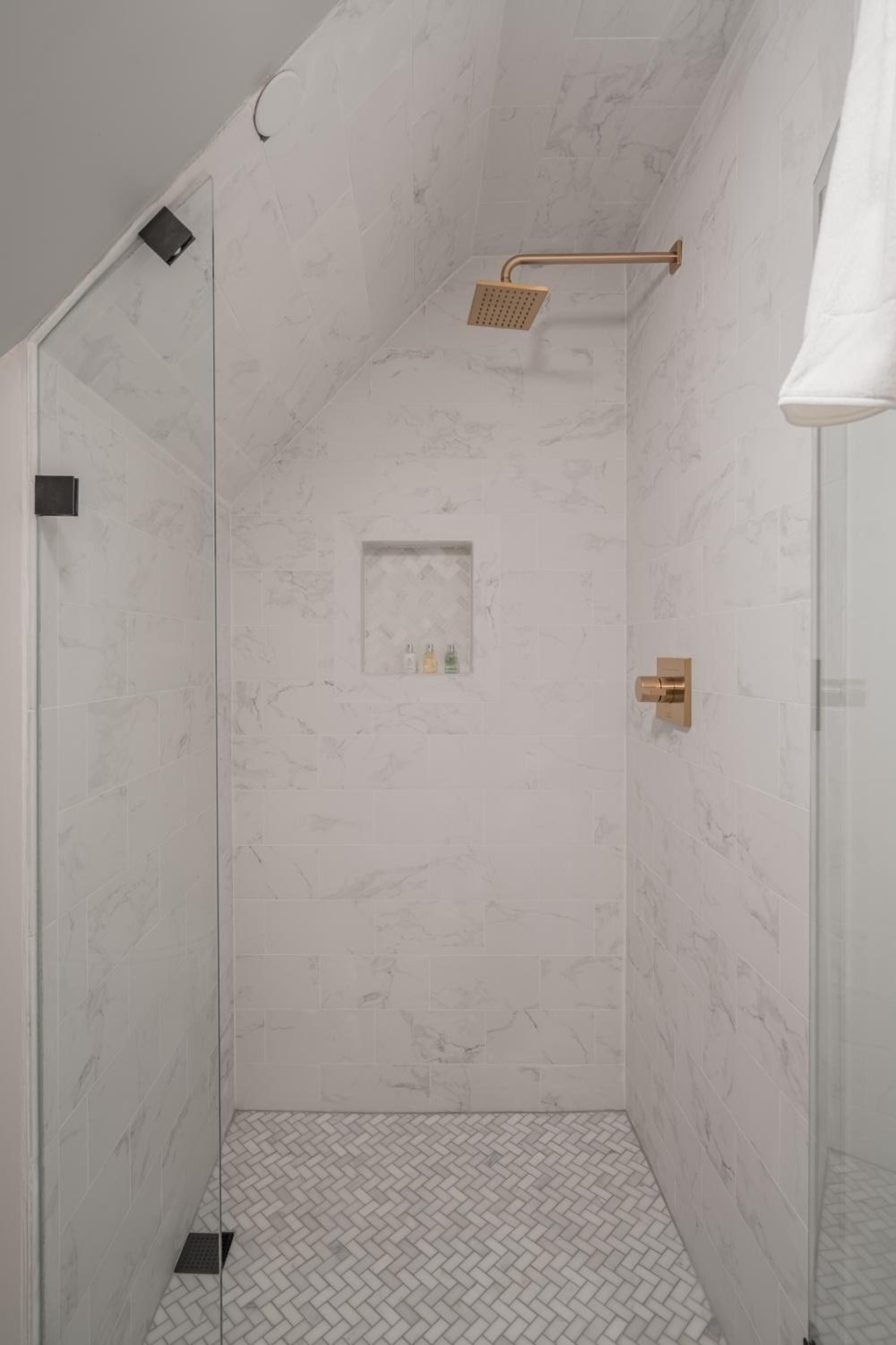 Crisp marble walls meet herringbone tile floors in this sophisticated shower sanctuary, where copper fixtures add warmth to the cool stone palette.