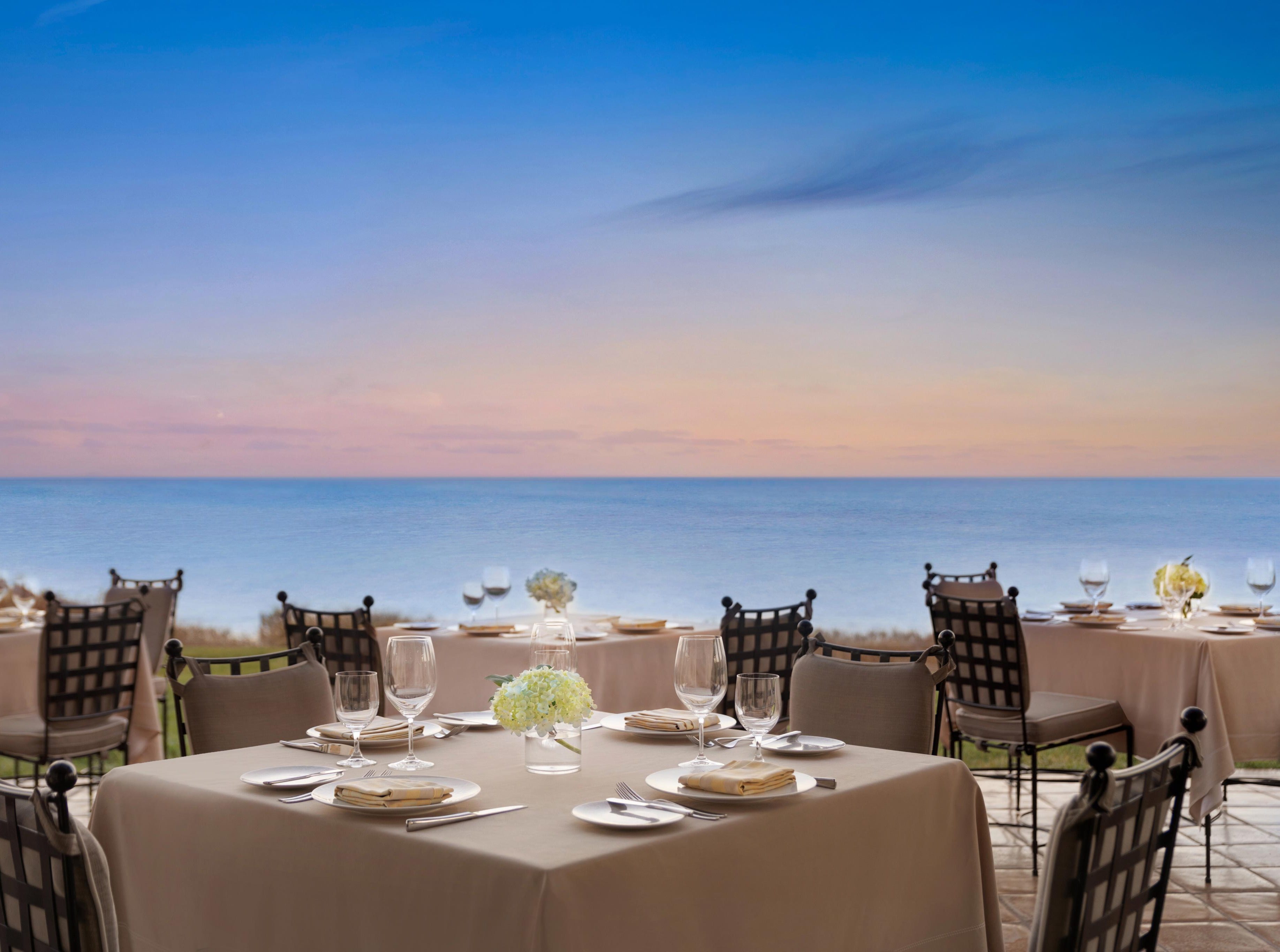 Sunset paints the Pacific horizon in soft pastels as elegant oceanfront tables await diners on Terranea's clifftop terrace, where coastal breezes mingle with culinary anticipation.