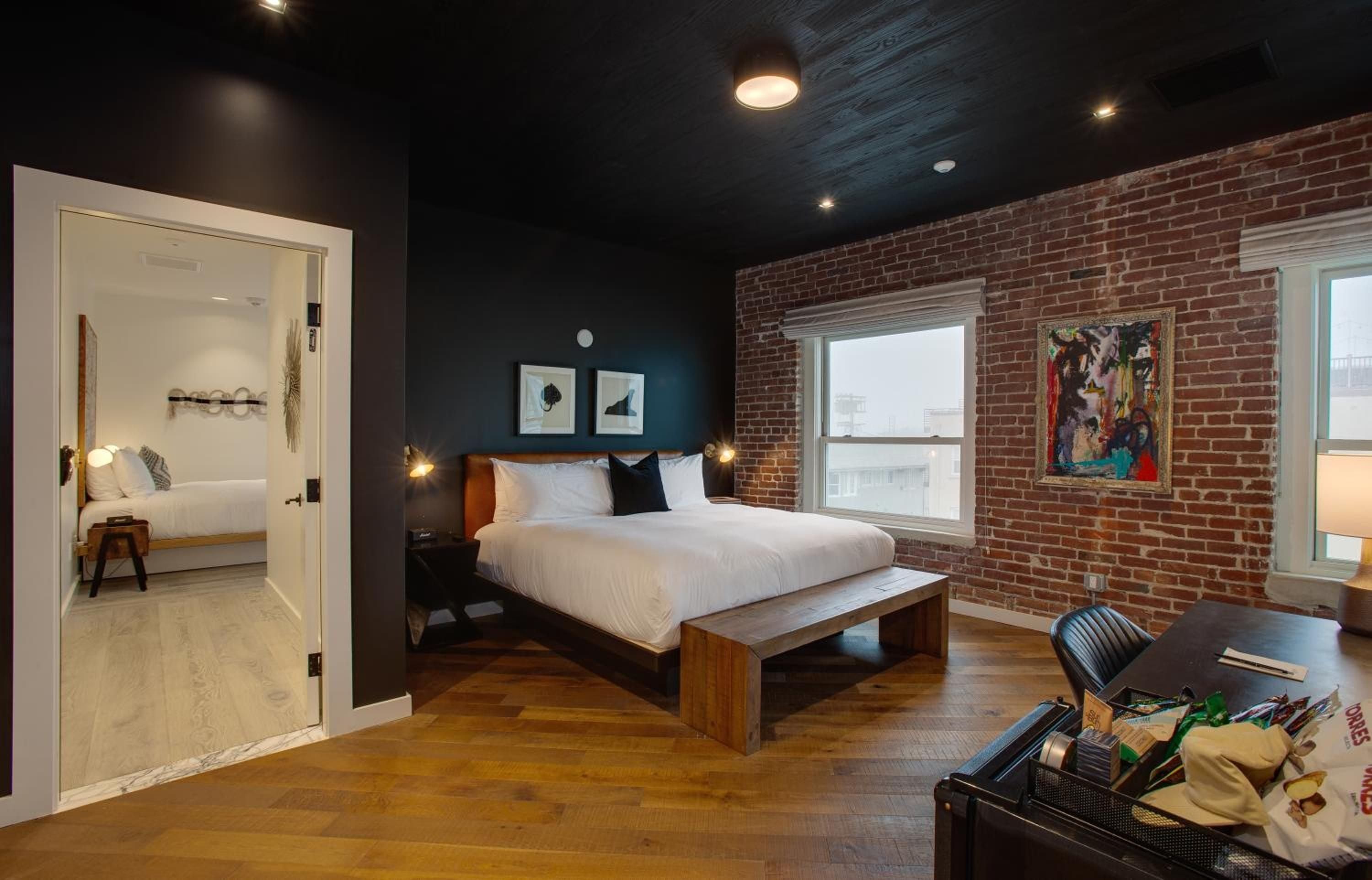 Exposed brick walls and dark wood floors create industrial warmth in this sophisticated suite, where modern platform beds meet Edison bulb sconces and colorful contemporary art.