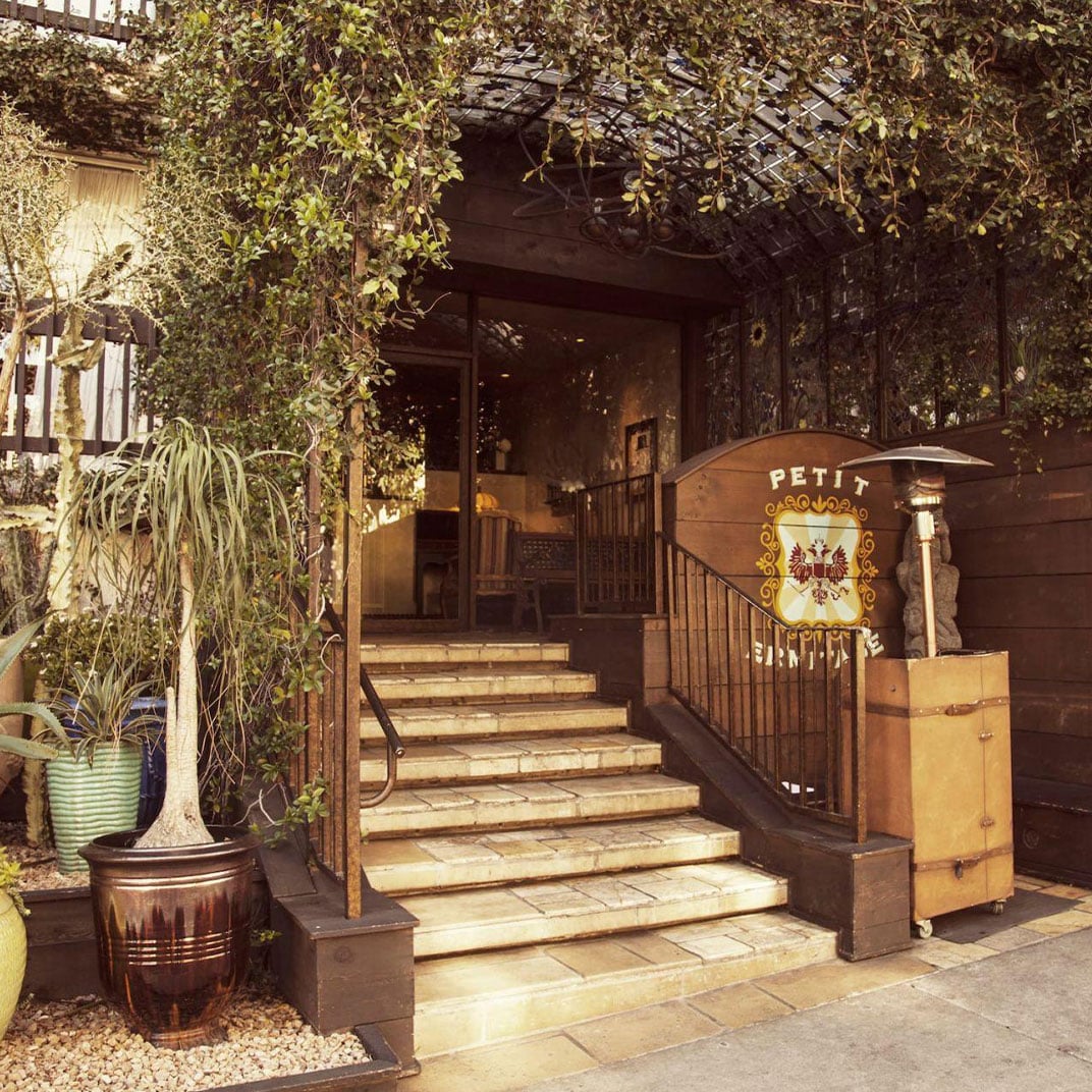 Stone steps wind through ivy-draped pergolas to reveal the hotel's intimate entrance, where weathered planters and vintage signage hint at hidden stories within.