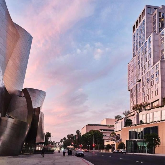 Frank Gehry's iconic Walt Disney Concert Hall curves gracefully beside Conrad Los Angeles as sunset paints downtown's skyline in shades of rose and lavender.