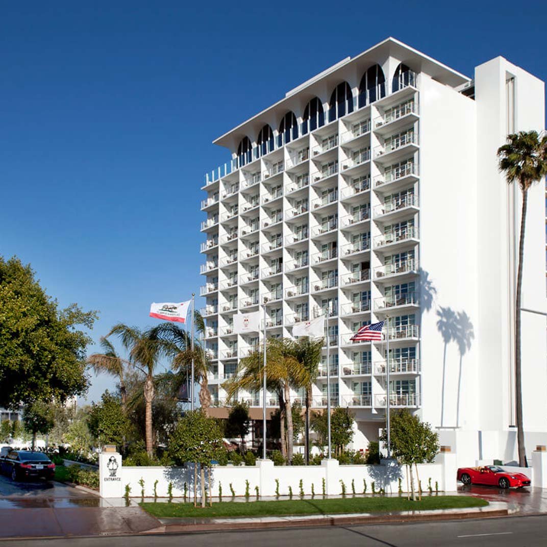 Mid-century modern elegance defines this pristine white facade, where distinctive arched windows and geometric balconies create striking shadows against Beverly Hills' perpetually blue sky.
