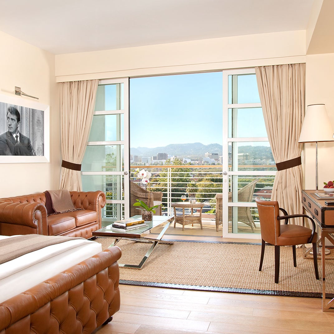 Tufted leather seating and warm wood tones create an inviting retreat, while floor-to-ceiling windows frame sweeping vistas of the Hollywood Hills beyond the private terrace.