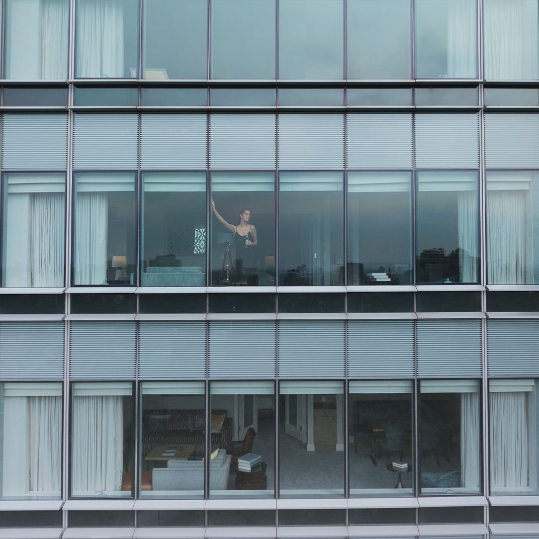 Floor-to-ceiling windows frame downtown Boston's urban tapestry, where a guest's silhouette catches afternoon light filtering through the hotel's sleek glass facade.