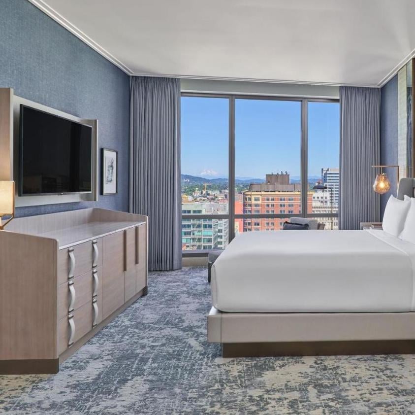 Floor-to-ceiling windows frame Portland's urban landscape from this sophisticated guest room, where blue accent walls complement crisp white linens and contemporary furnishings.