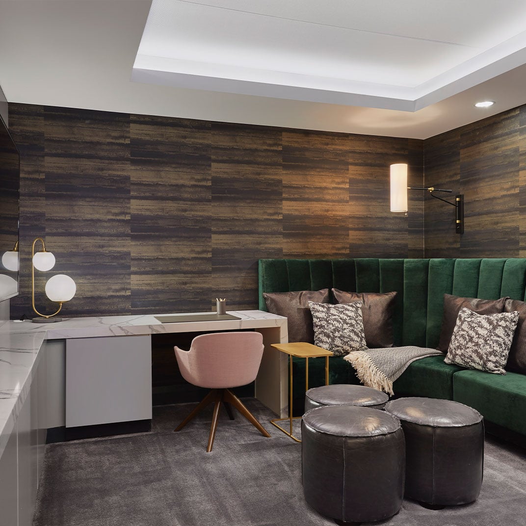 Emerald velvet seating contrasts beautifully with rich wood-paneled walls, while brass accents and a sleek marble desk create an intimate workspace within the sophisticated suite.