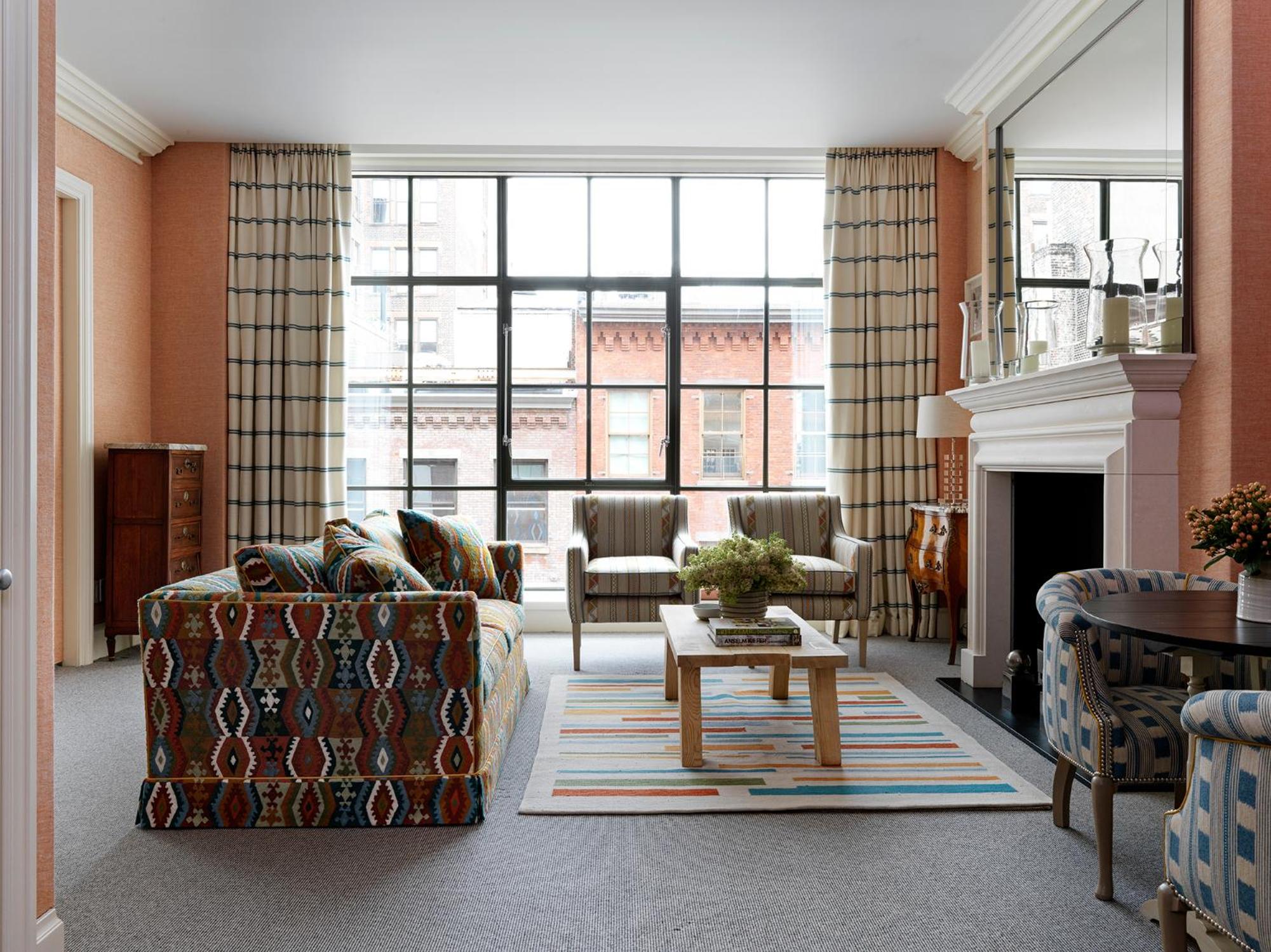 Kilim patterns and plaid upholstery create cheerful discord in this coral-washed sitting room, where oversized windows frame SoHo's industrial brick facades.