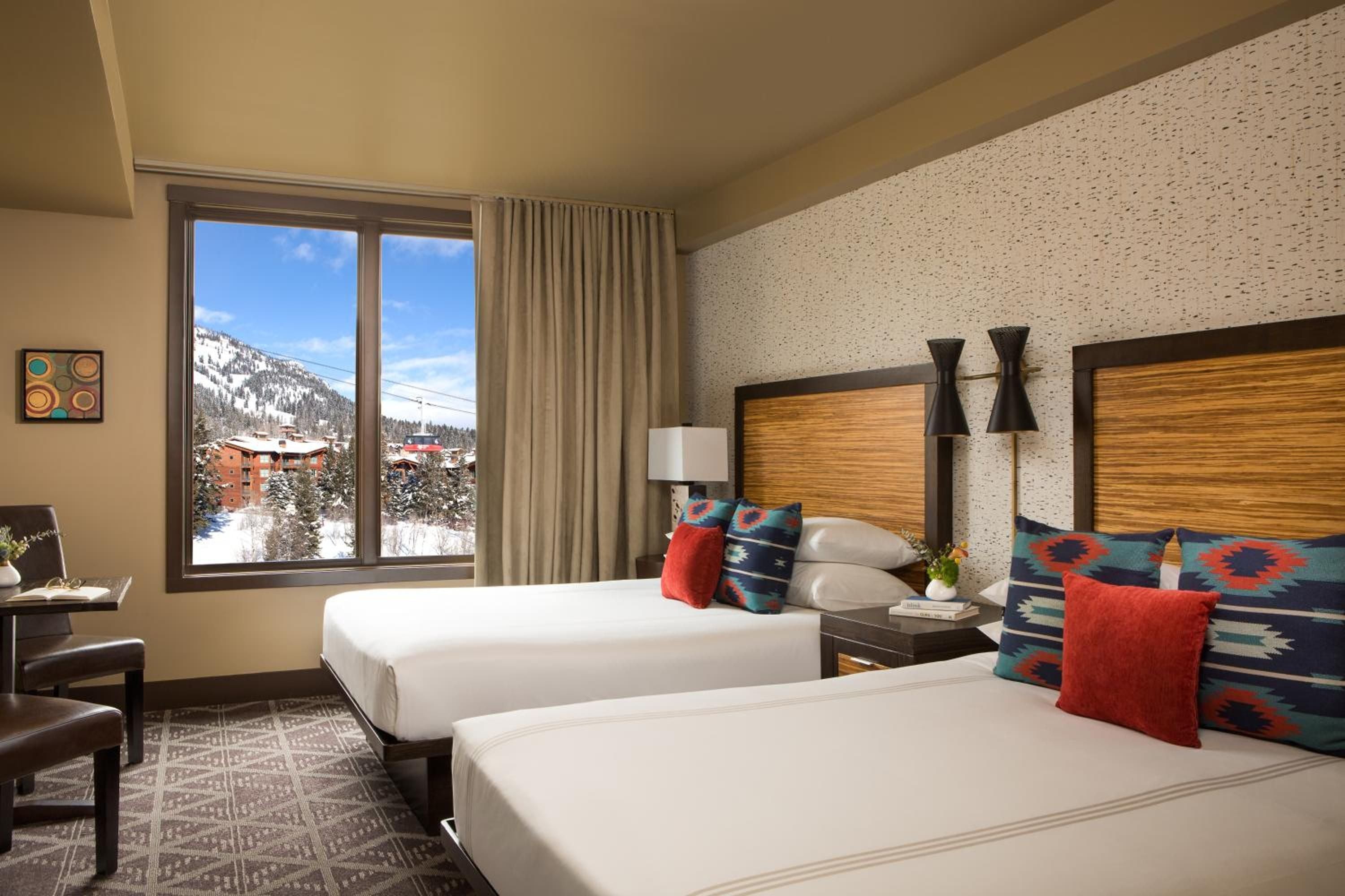 Twin beds dressed in geometric Southwestern textiles frame snow-dusted peaks through floor-to-ceiling windows, where mountain light warms wood headboards and speckled accent walls.