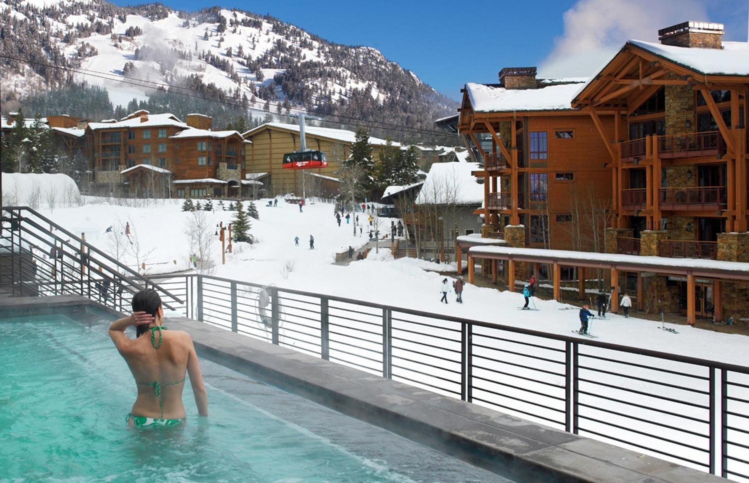Steam rises from heated waters as a guest soaks in the infinity pool, snow-dusted ski slopes and timber lodges creating a striking Alpine backdrop.