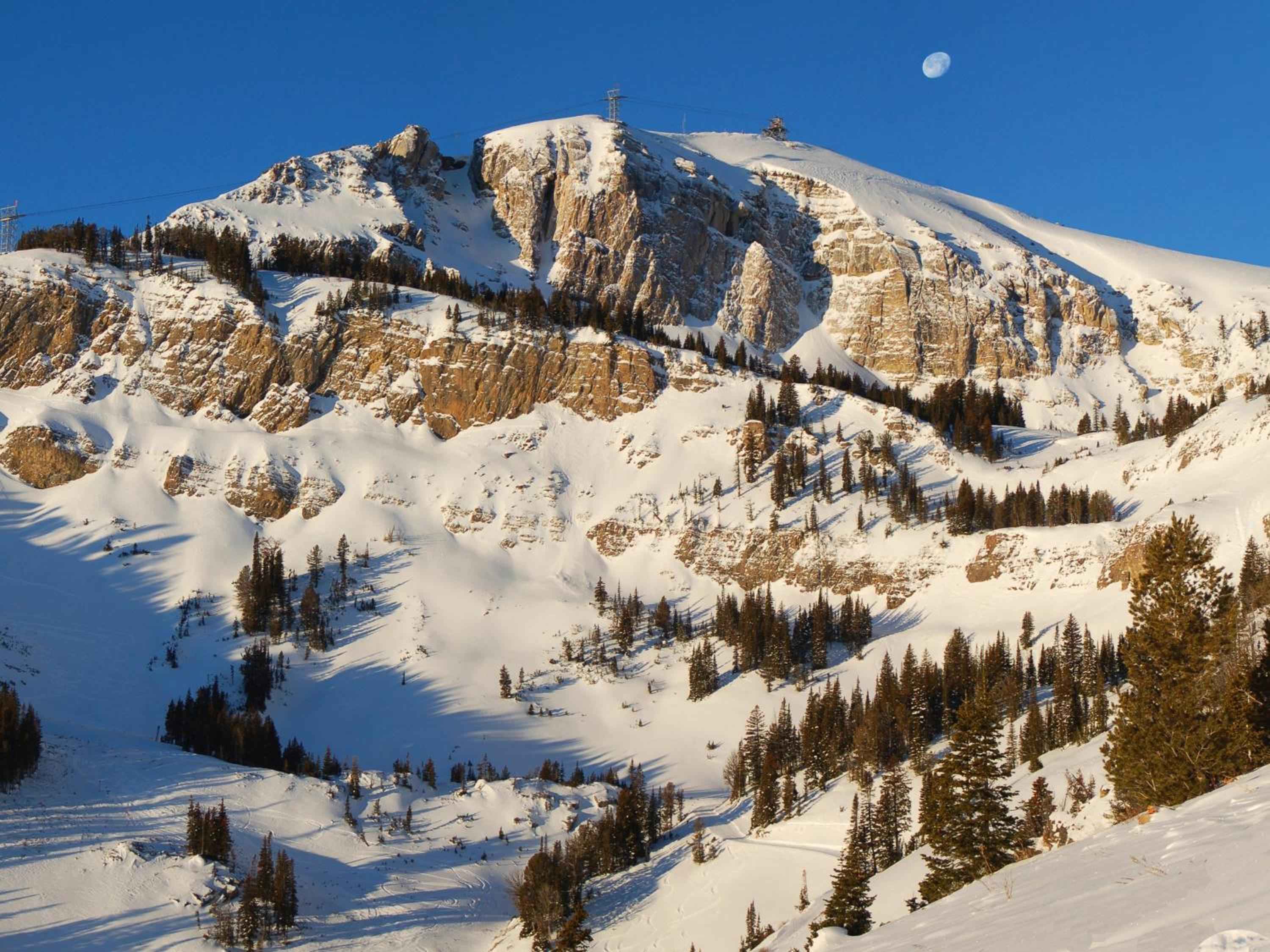 Snow-draped limestone cliffs rise majestically beyond the lodge, where moonlit peaks and pristine powder create Jackson Hole's most dramatic alpine backdrop.
