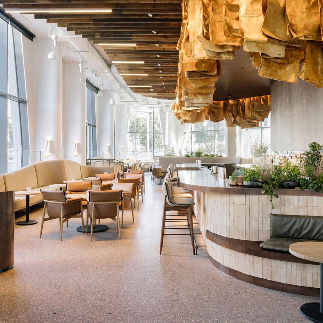 Warm terrazzo floors and an unexpected canopy of weathered paper bags create intimate conversation nooks beneath soaring timber beams and industrial-chic lighting.