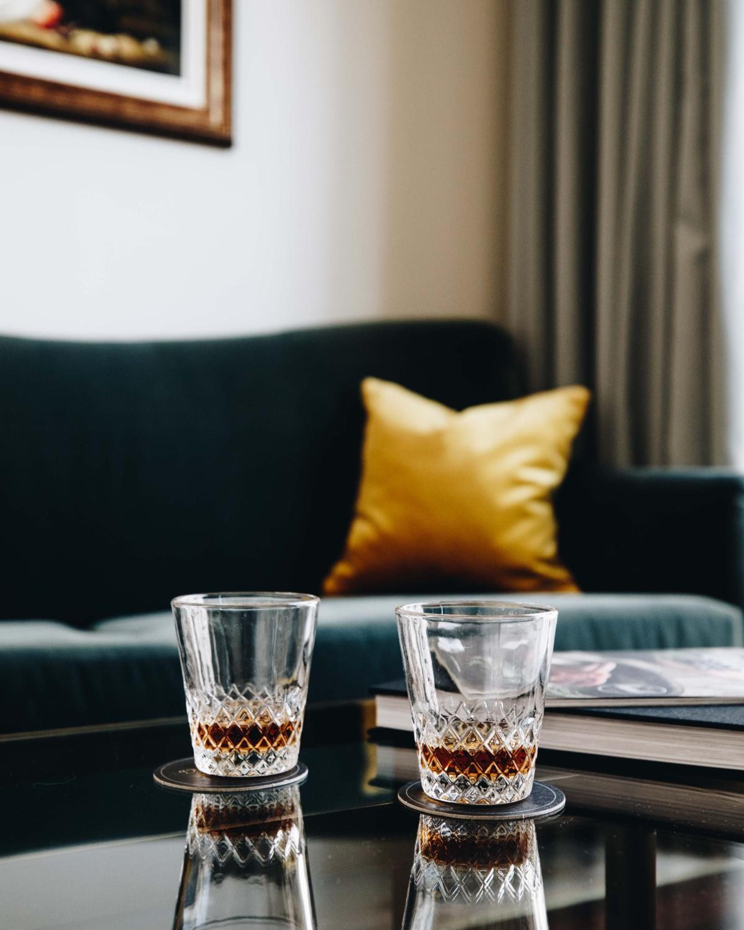 Crystal cut glasses catch afternoon light on polished surfaces, while emerald velvet and golden silk create an intimate corner perfect for evening whiskey rituals.