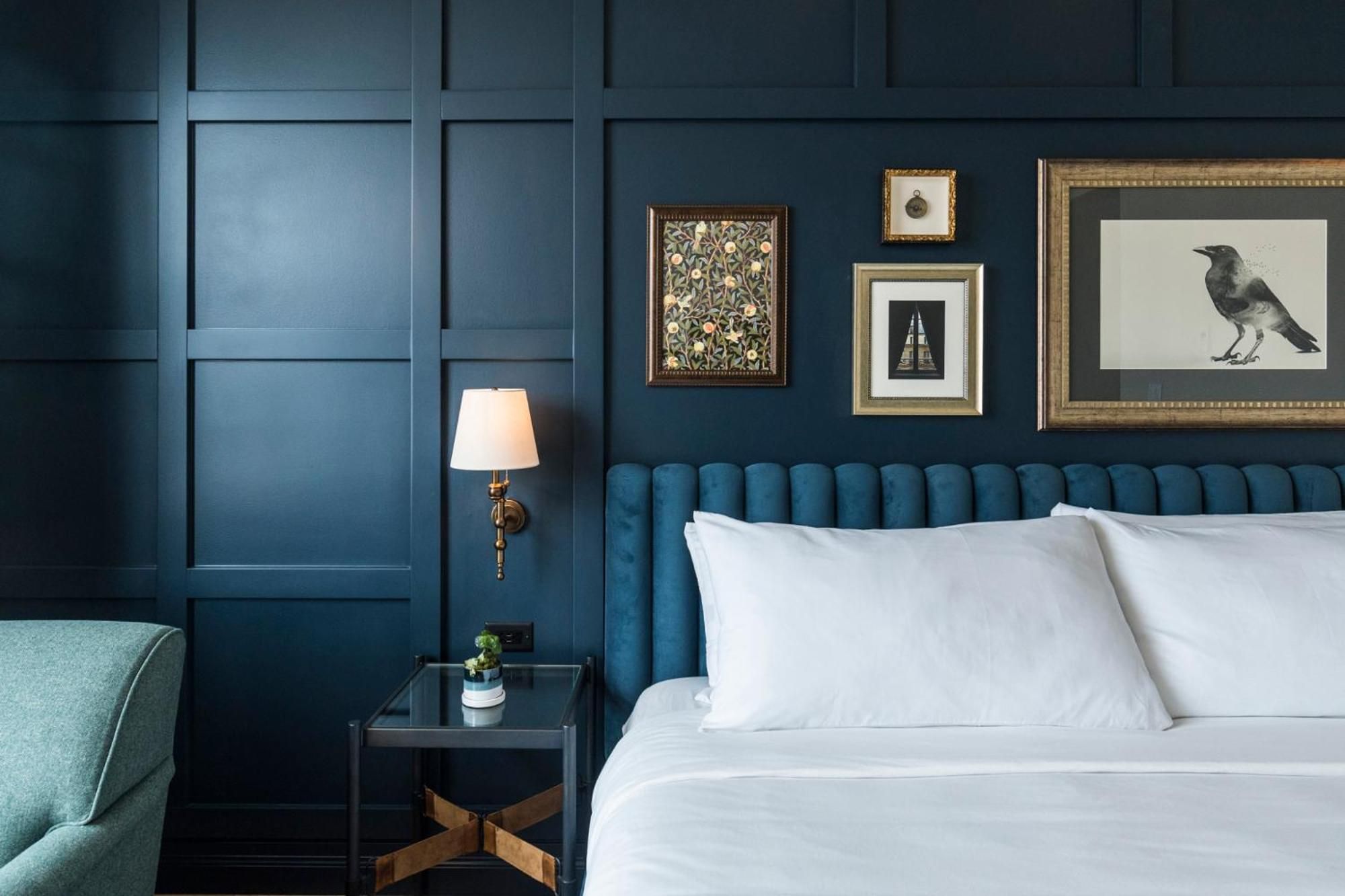 Rich navy paneling and gilded frames create an intimate sanctuary, where brass sconces cast warm light across crisp linens and a tufted velvet headboard.