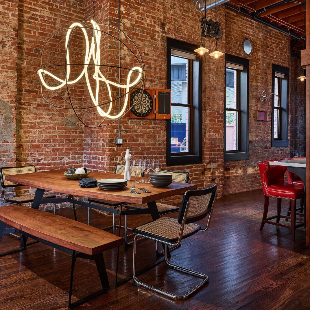 Exposed brick walls and sculptural lighting create intimate dining moments, where cane-backed chairs gather around walnut tables set with artisanal ceramics and gleaming glassware.