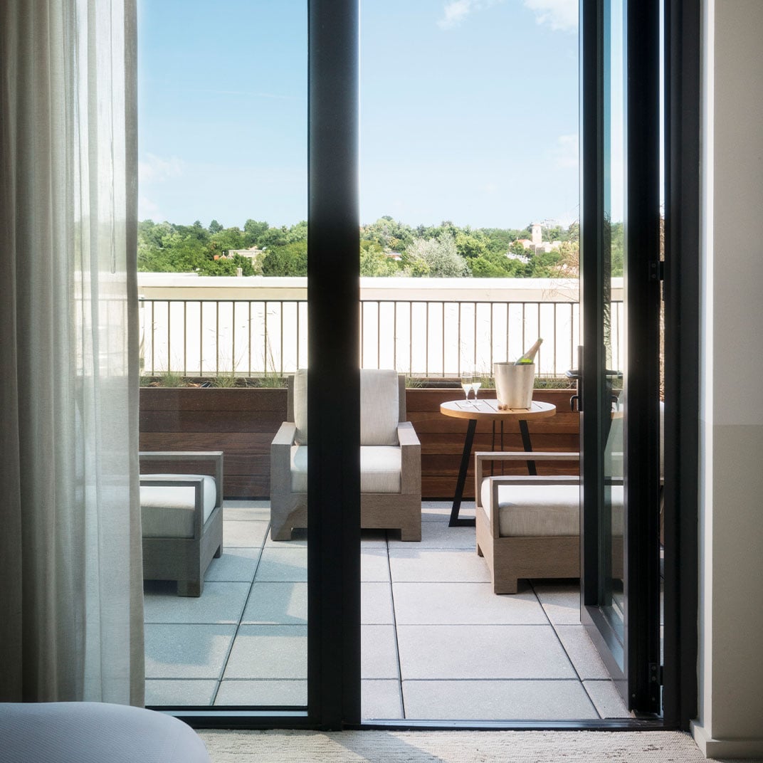 Floor-to-ceiling windows frame a private terrace where teak furniture invites lingering over morning coffee, with verdant treetops stretching toward the horizon.