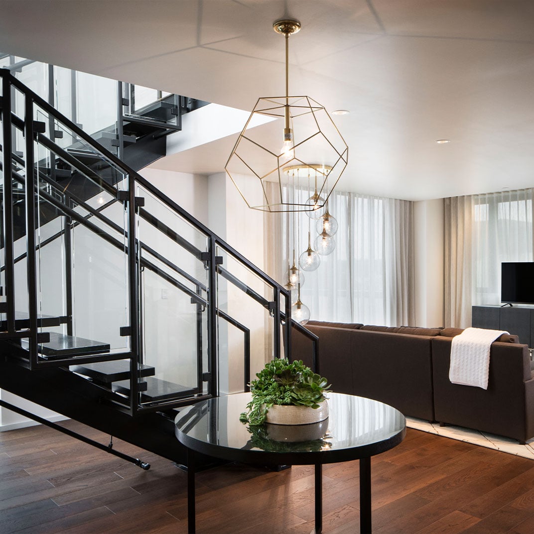 Geometric brass fixtures cast warm light over sleek black railings and polished surfaces, where modern industrial design meets sophisticated residential comfort in the open-plan living space.